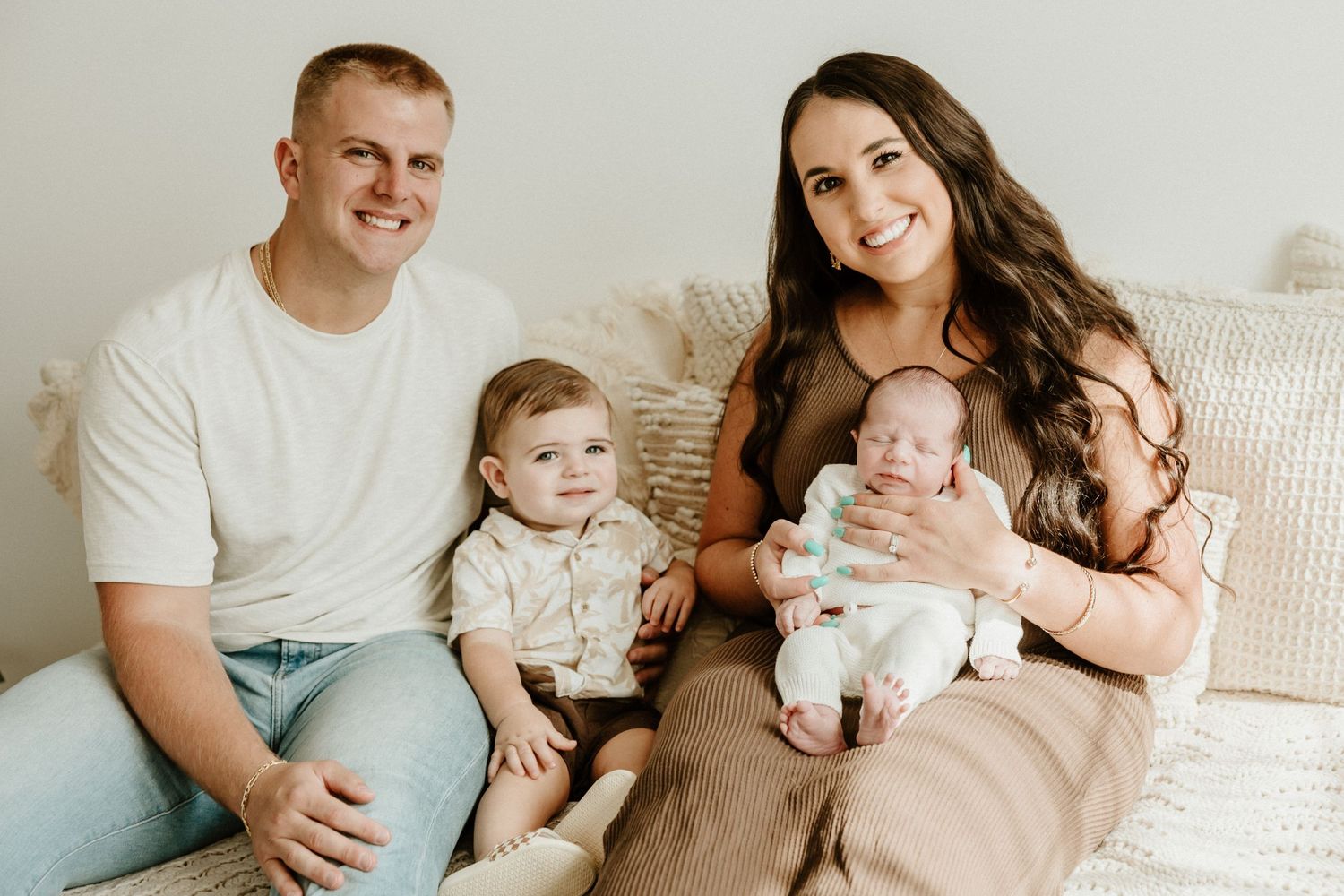 A relaxed family portrait on a cozy couch with neutral tones and soft lighting.