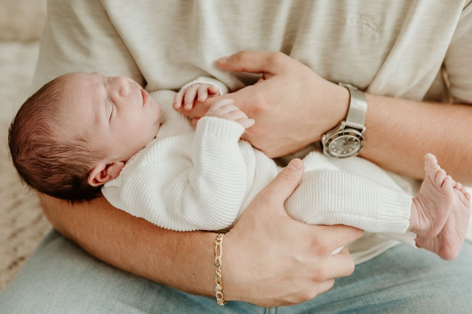 A sleeping newborn baby cradled in gentle hands wearing a white onesie.