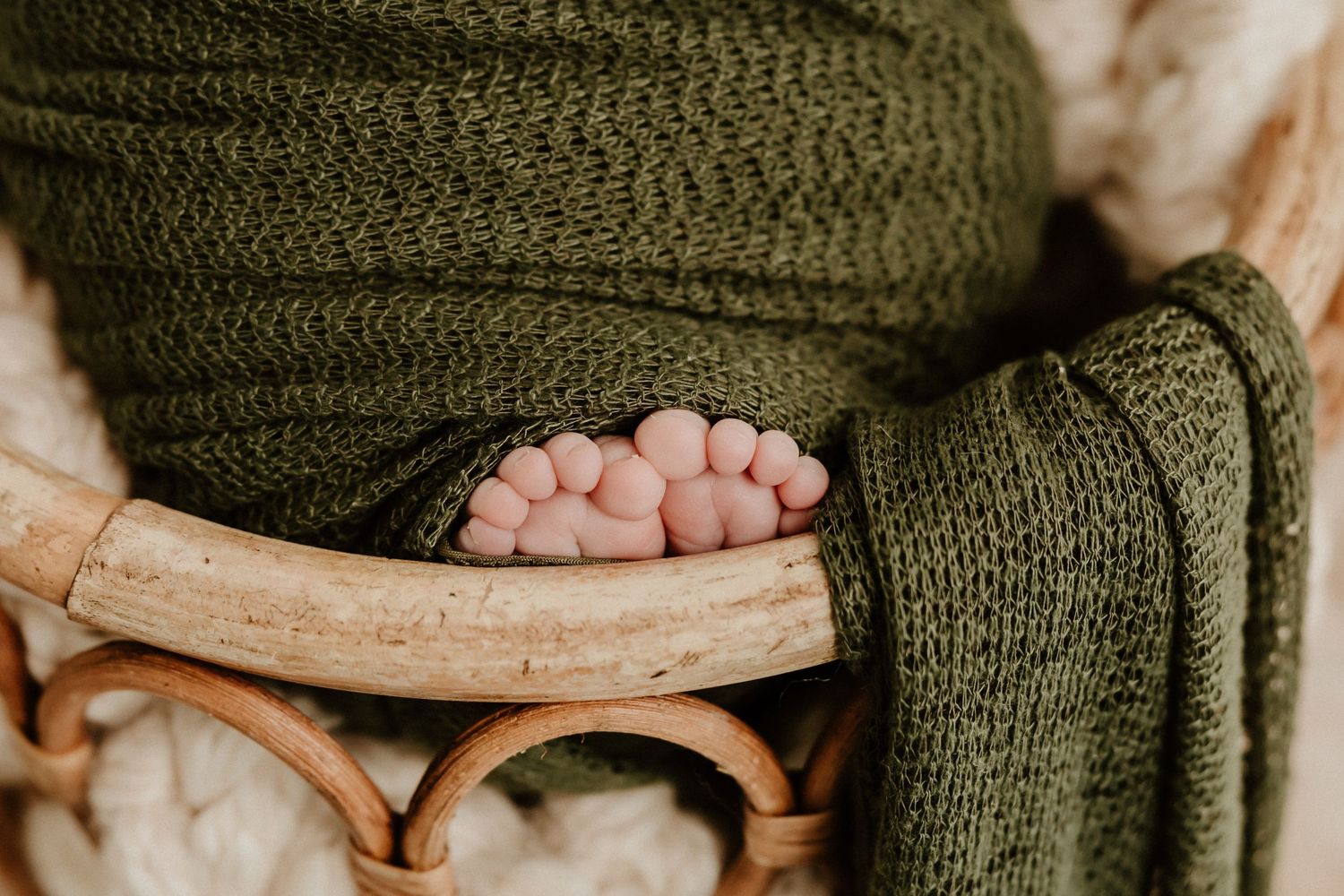 Tiny baby toes peek out from a cozy olive green knit blanket resting on wooden furniture.