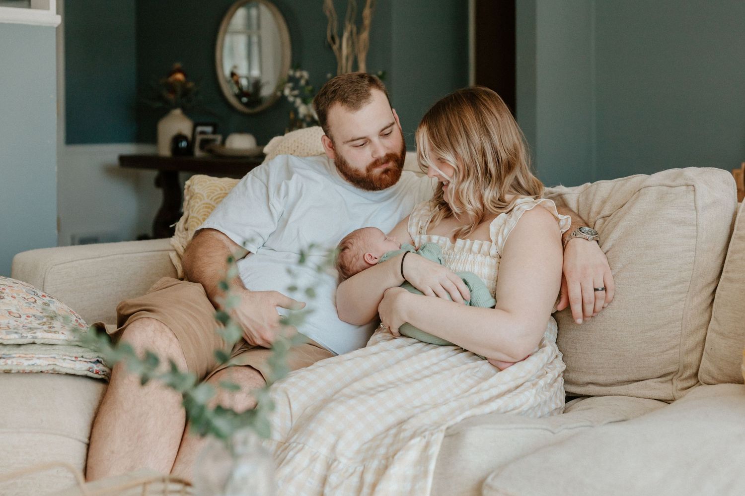 Intimate family moment on a cozy gray couch with newborn baby.