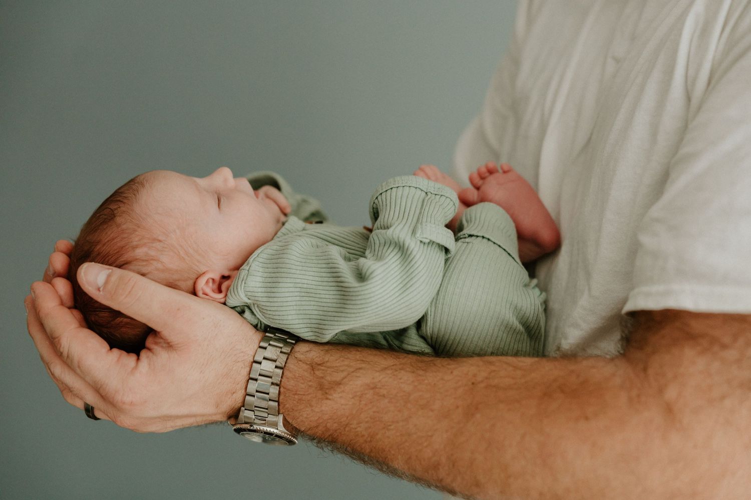 Gentle hands holding a sleeping newborn wearing soft mint green outfit.