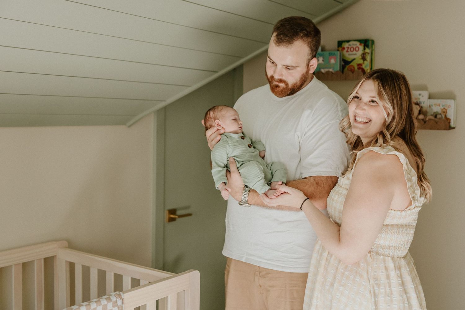 Family of three sharing a tender moment in mint-colored nursery.