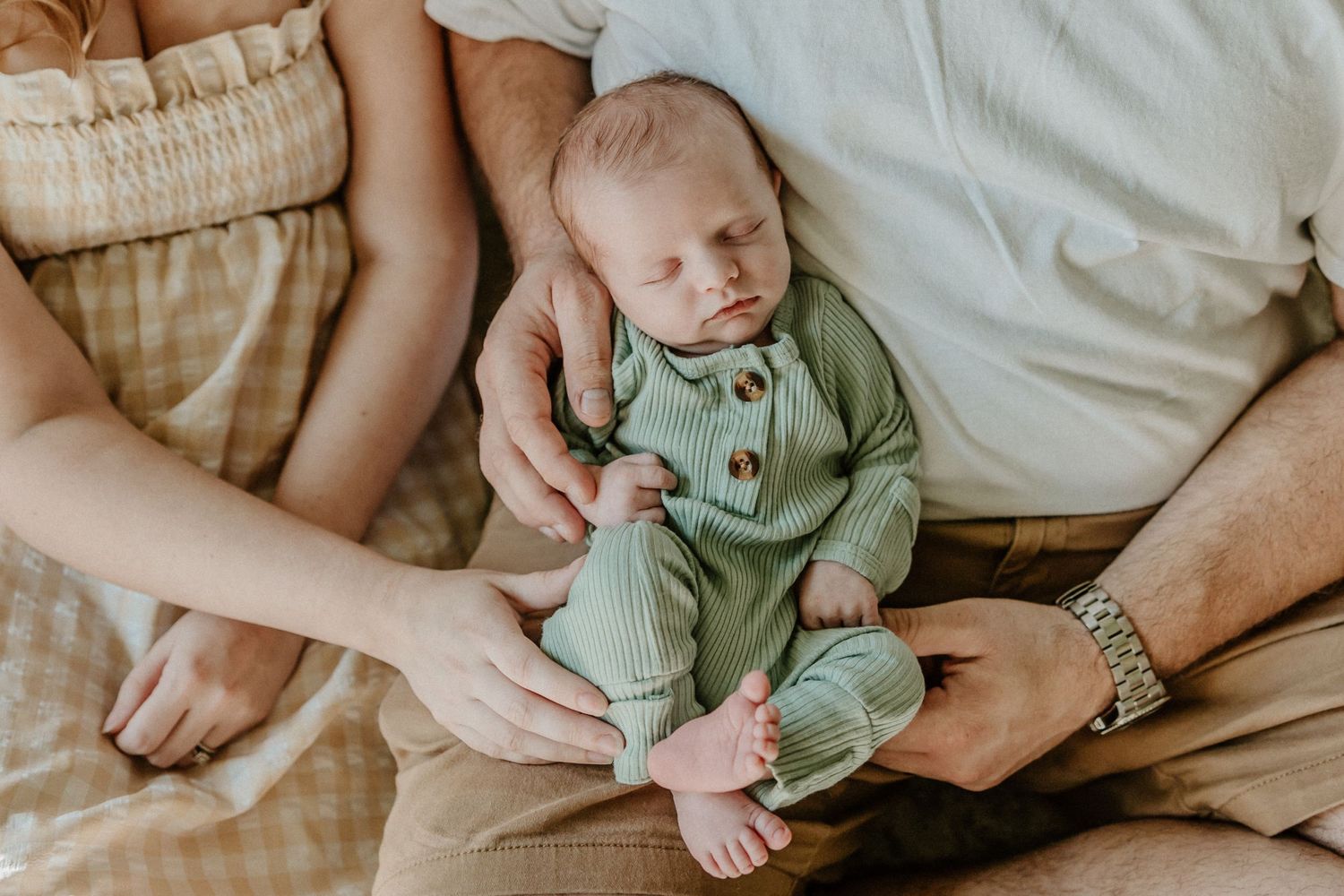 Newborn in mint green romper resting on soft beige bedding.
