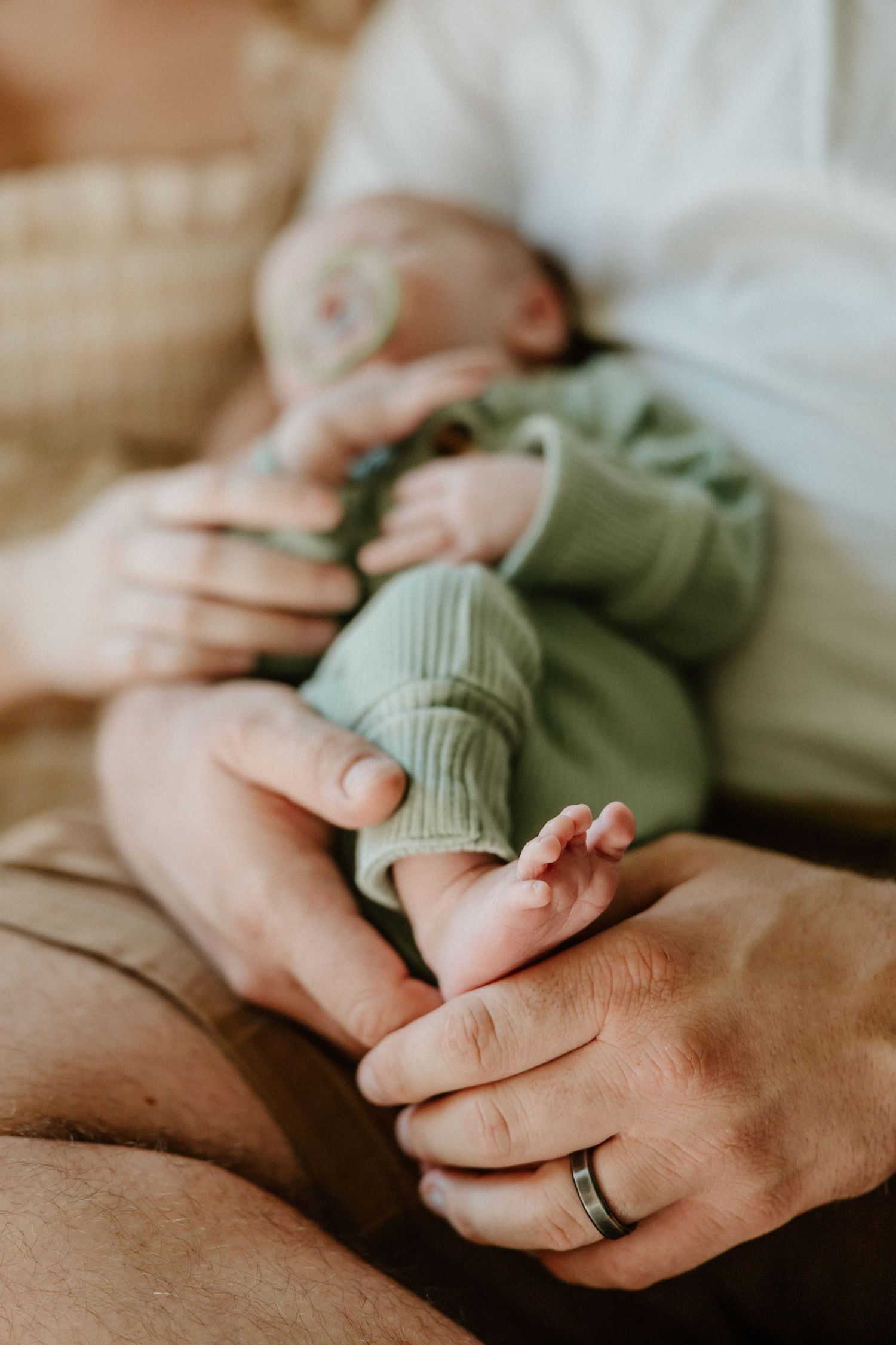 Close-up of tiny newborn feet in mint green outfit while being held.