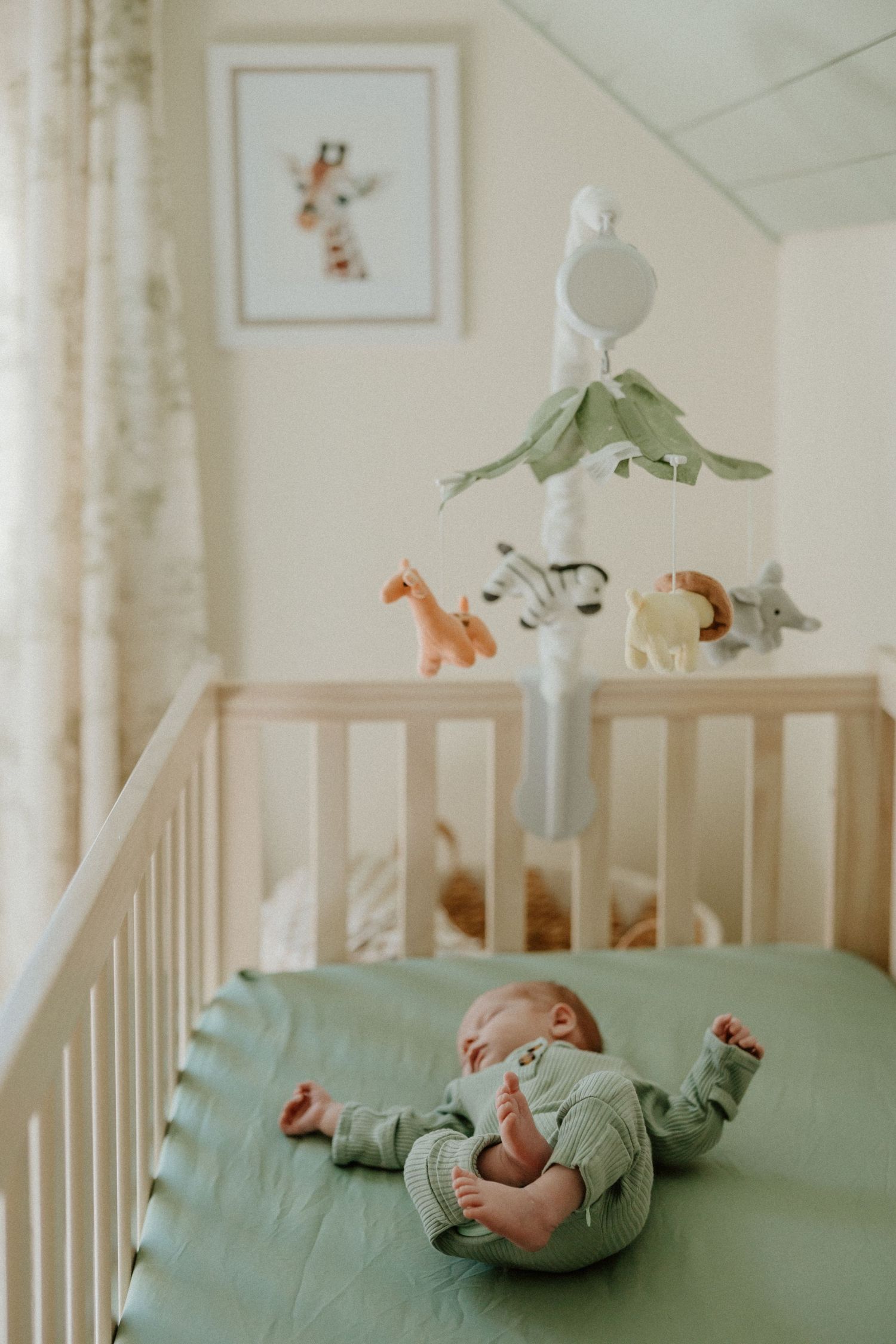Baby lying on mint green bedding in a white crib with animal mobile hanging above.