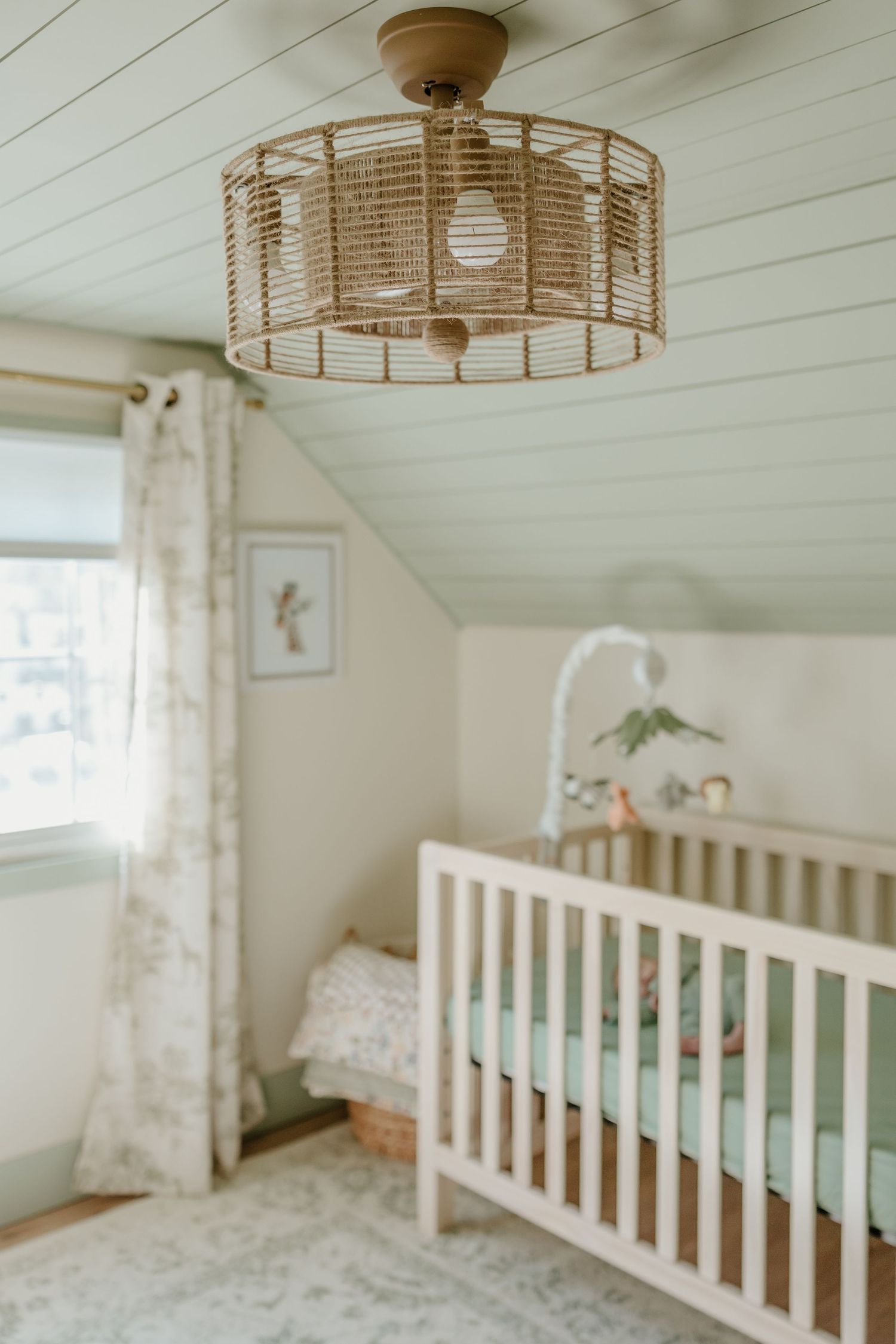 Modern nursery with white crib, woven ceiling light, and sheer curtains in a peaceful setting.