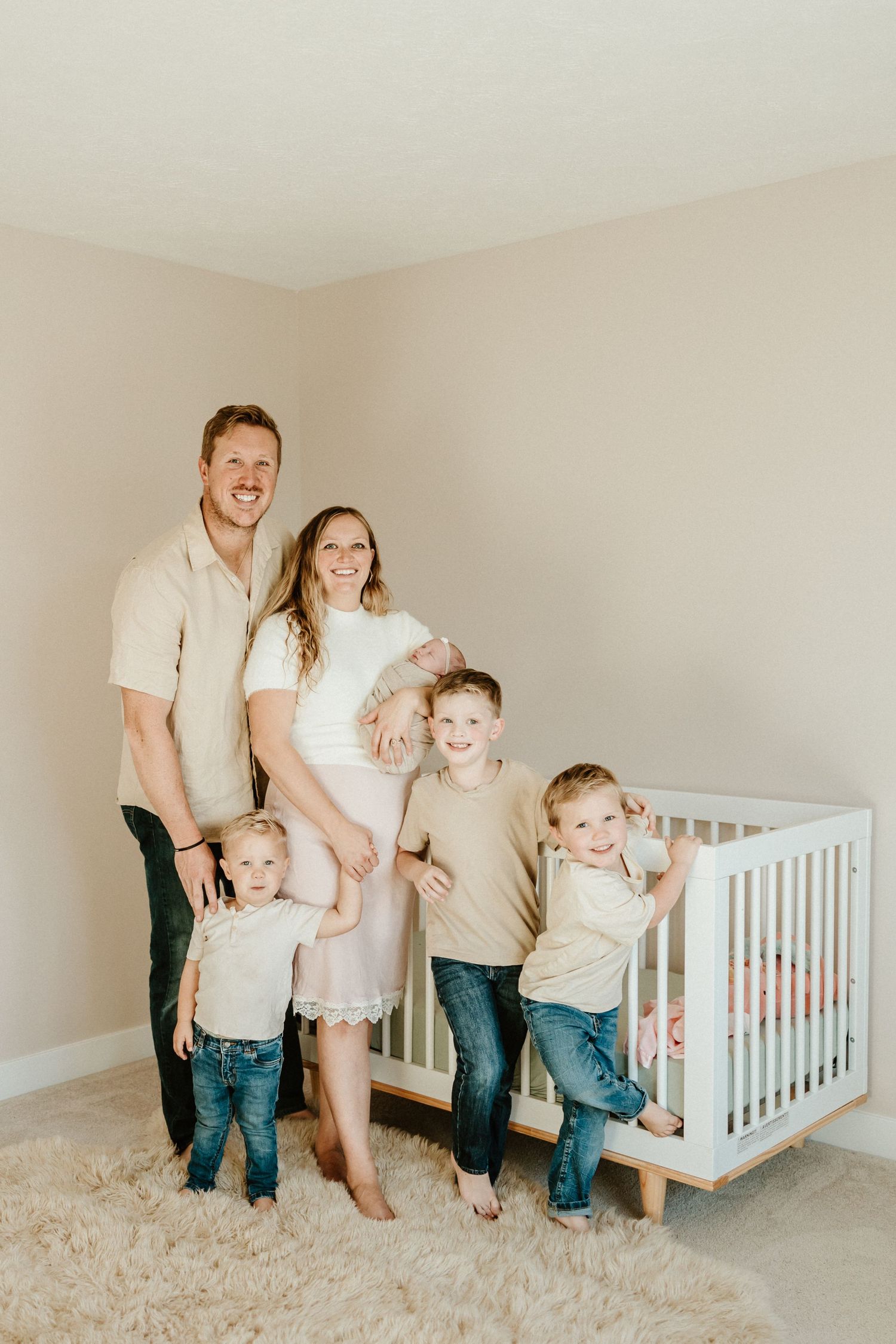 Family portrait in neutral colors standing together in nursery with white crib.
