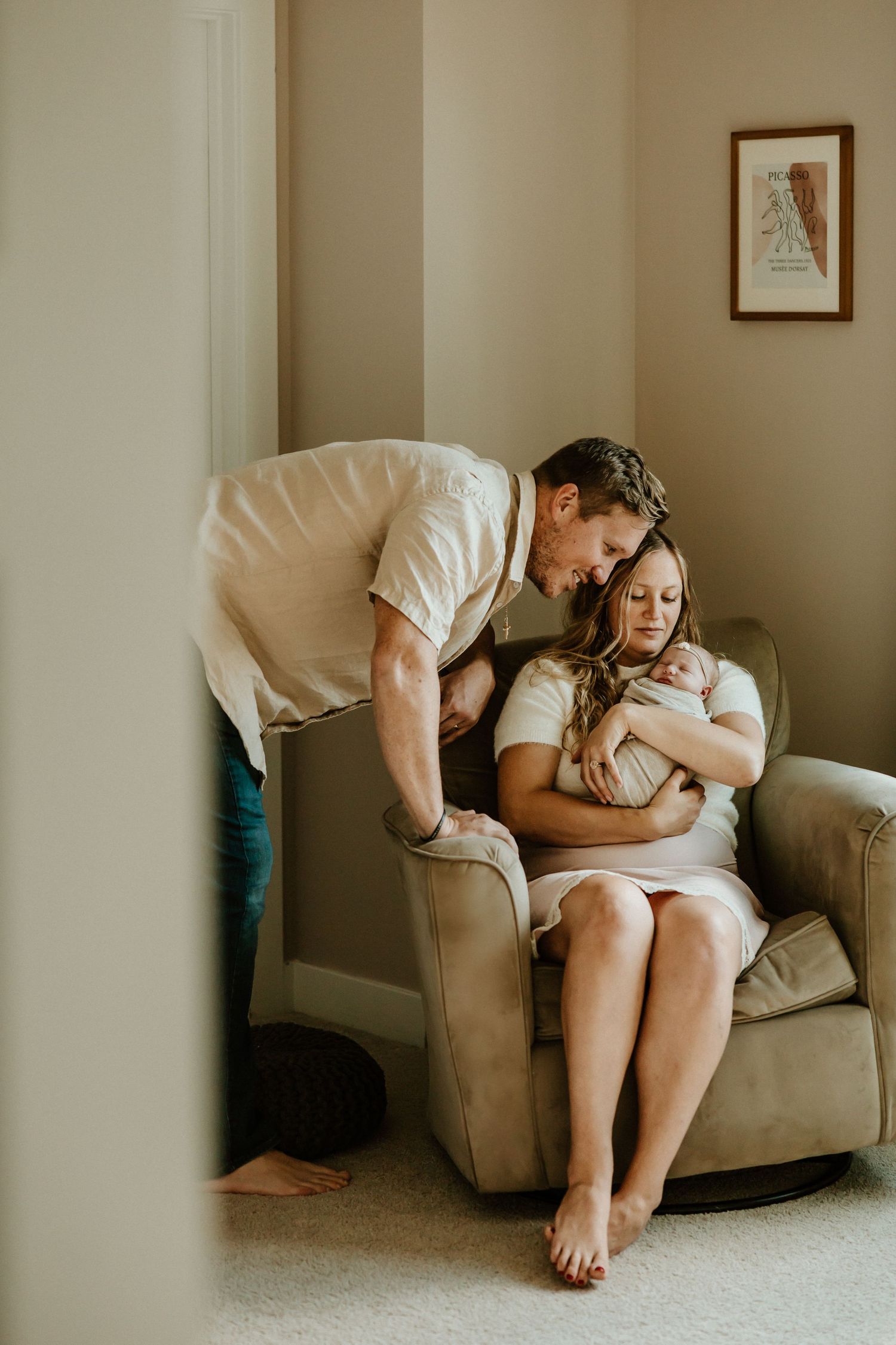 Tender family moment captured through doorway in neutral-toned nursery setting.