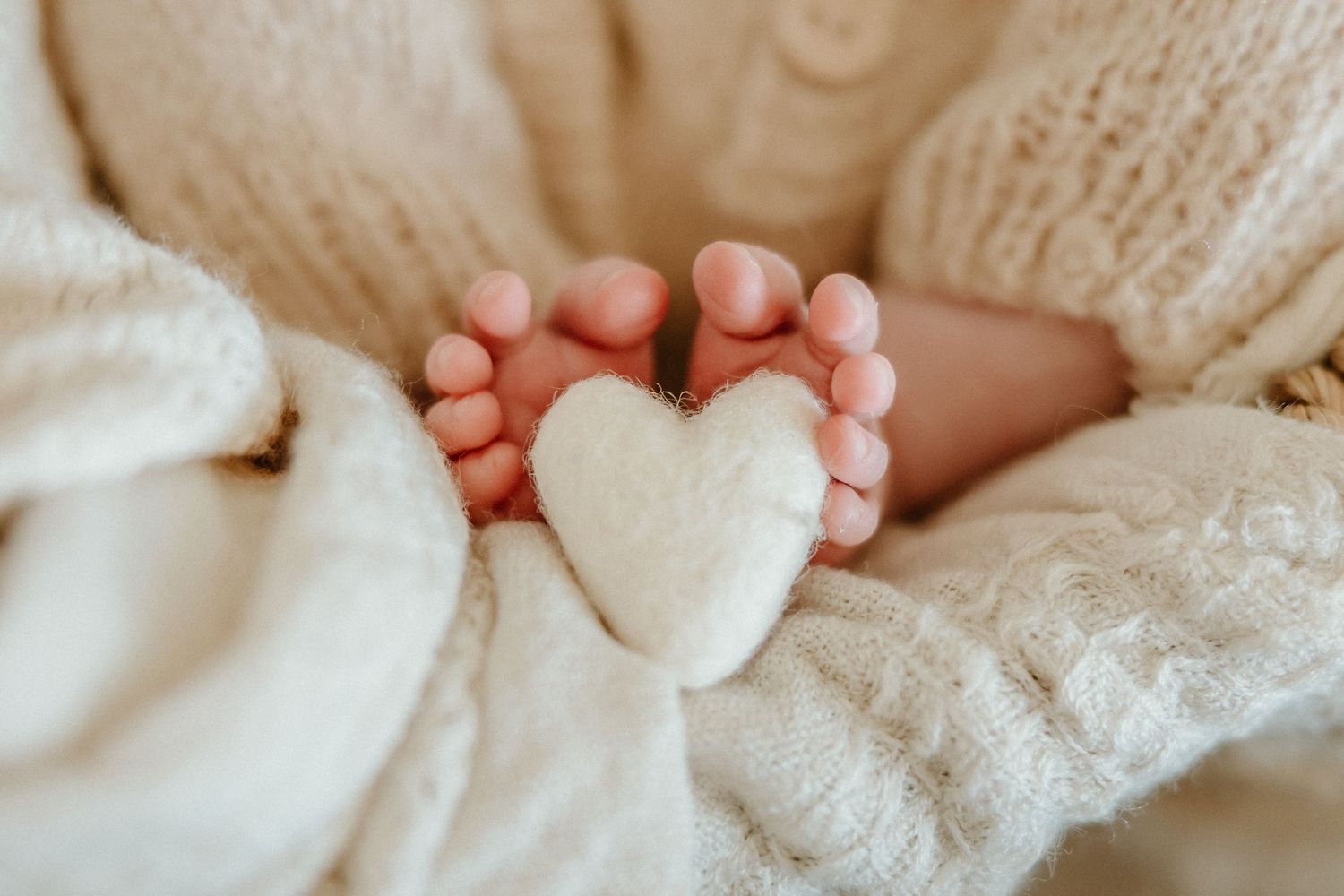 Tiny baby feet forming a heart shape with white plush heart between them.