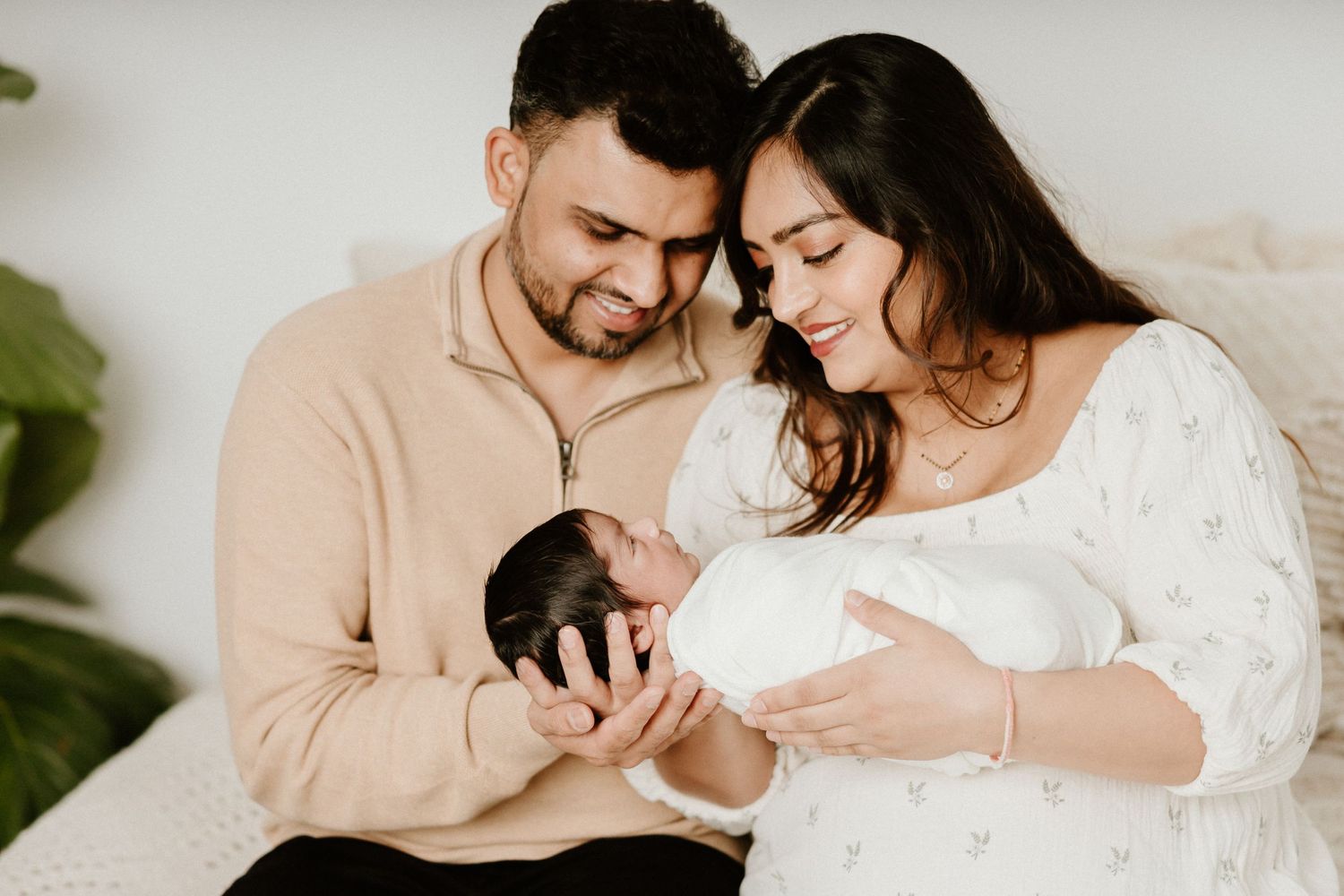 New parents tenderly hold their newborn baby in an intimate indoor portrait.