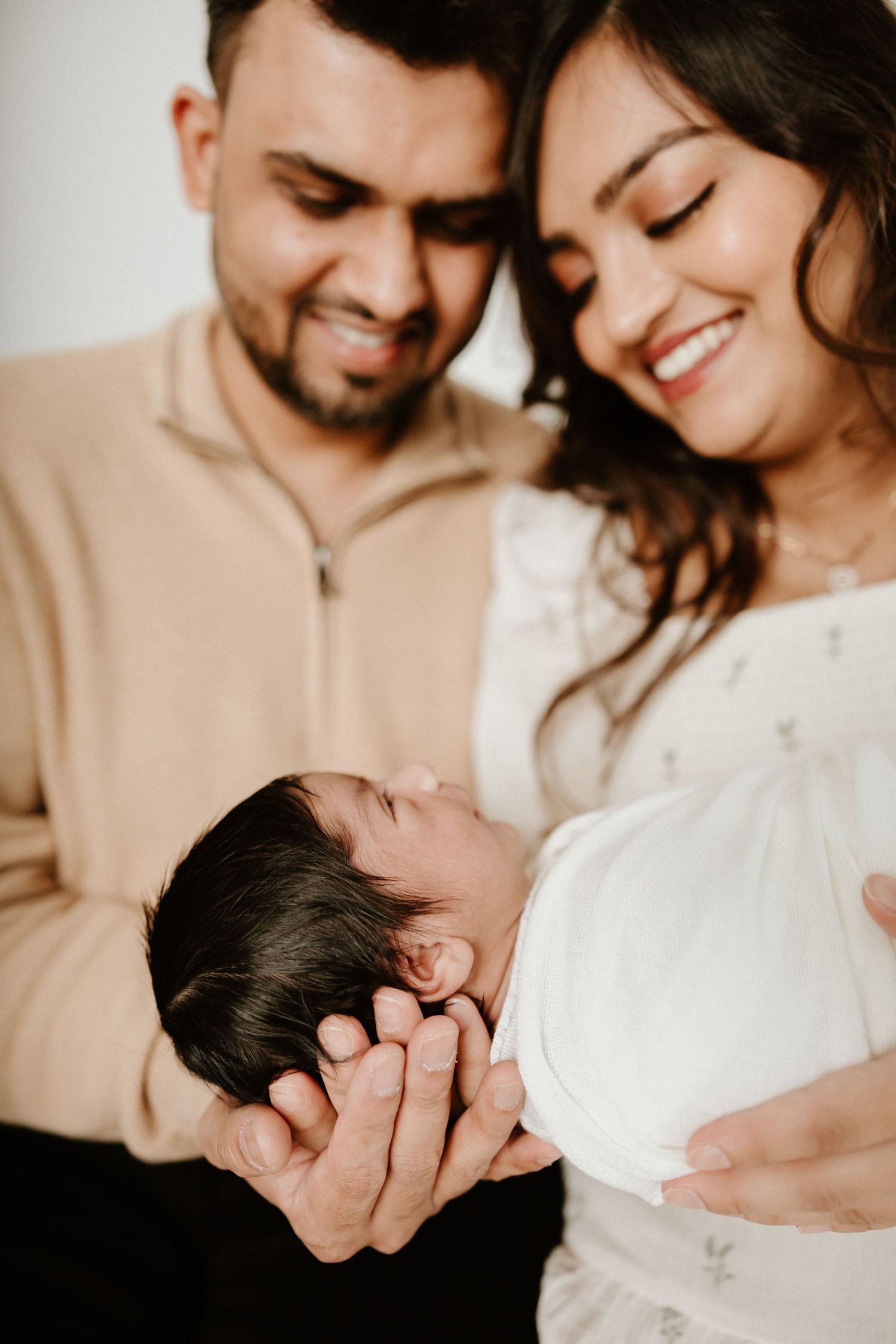 Parents share a tender moment with their sleeping newborn in casual home setting.