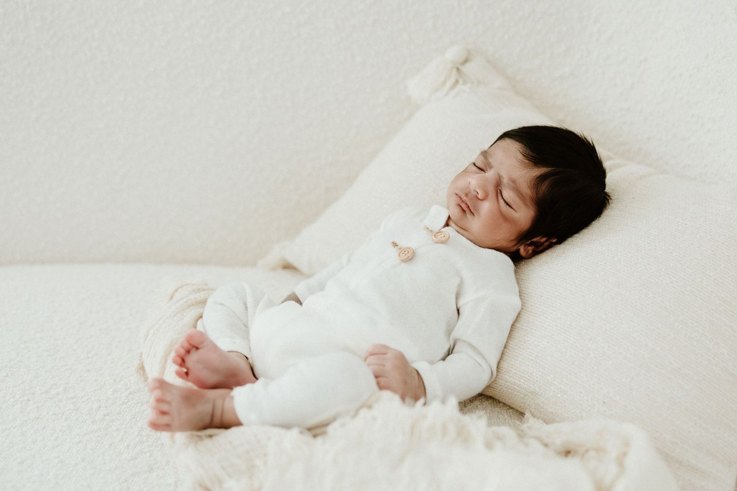 Peaceful sleeping newborn in white outfit rests on light bedding.