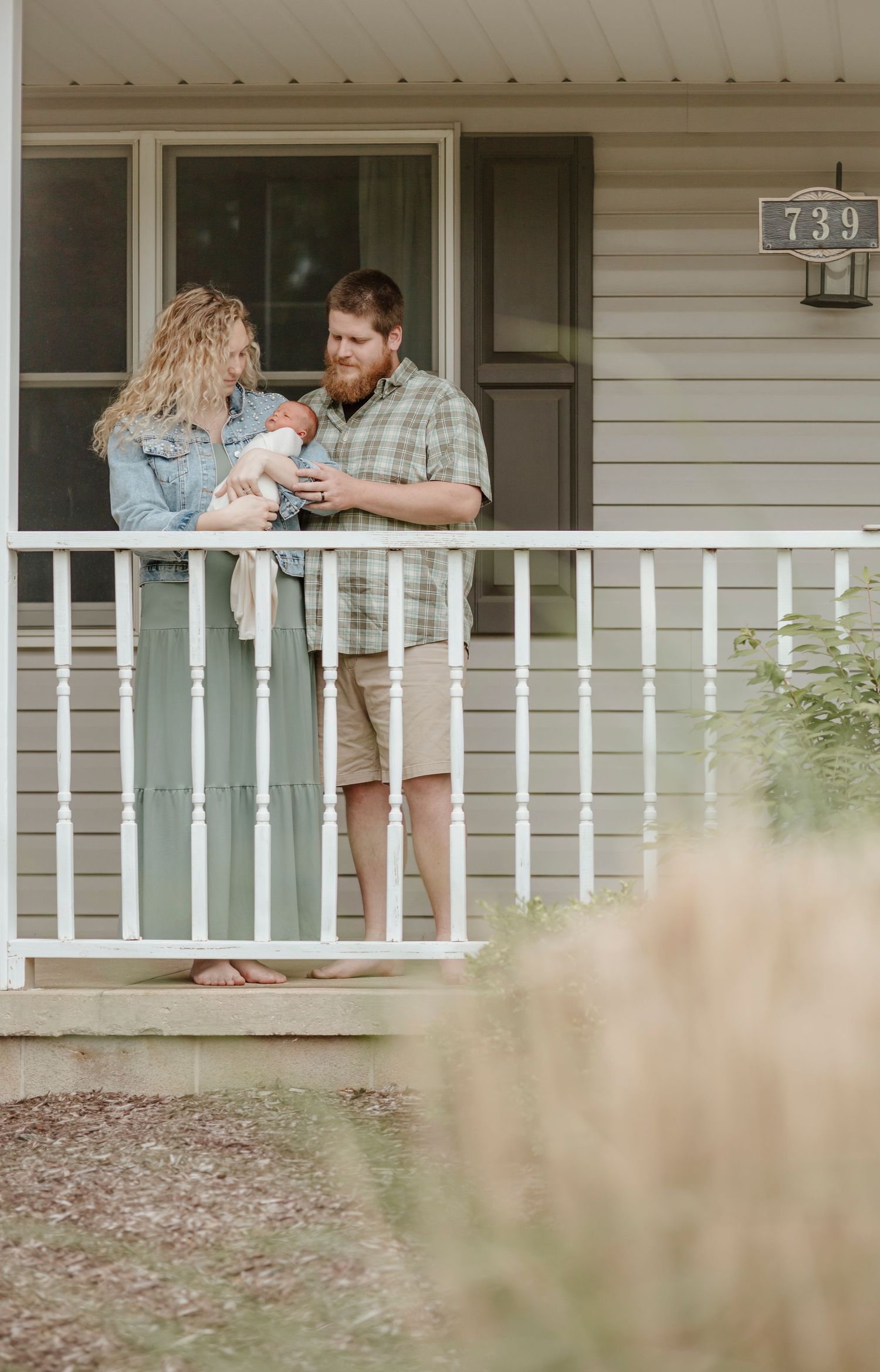 A couple standing on their front porch with their newborn at house number 739.