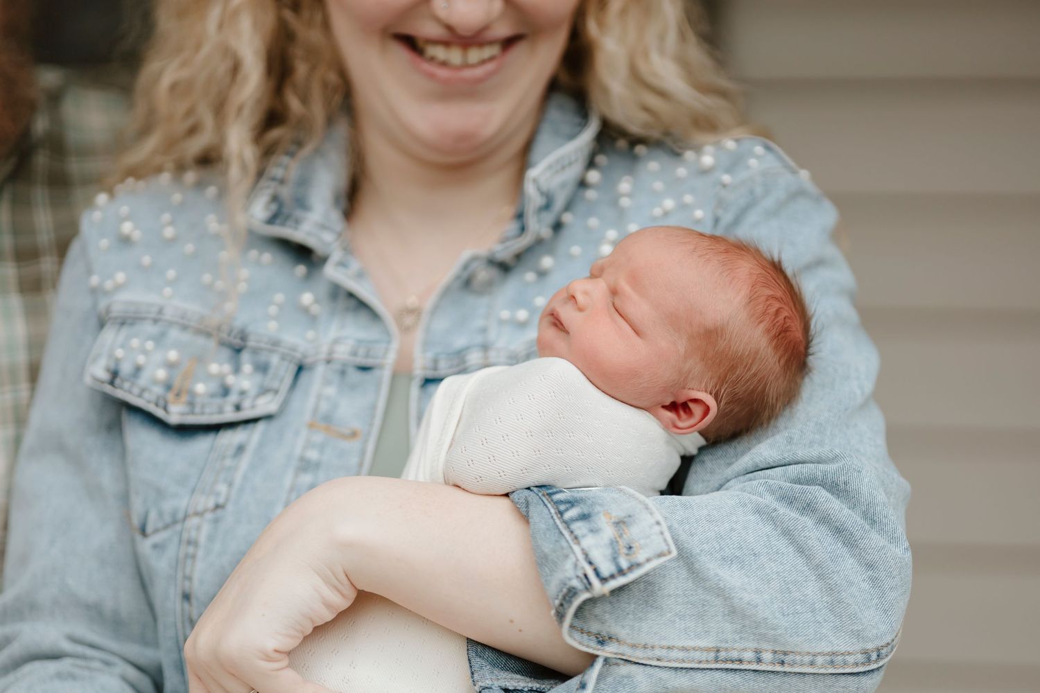 A newborn in white clothing sleeping peacefully in someone's denim-clad arms.