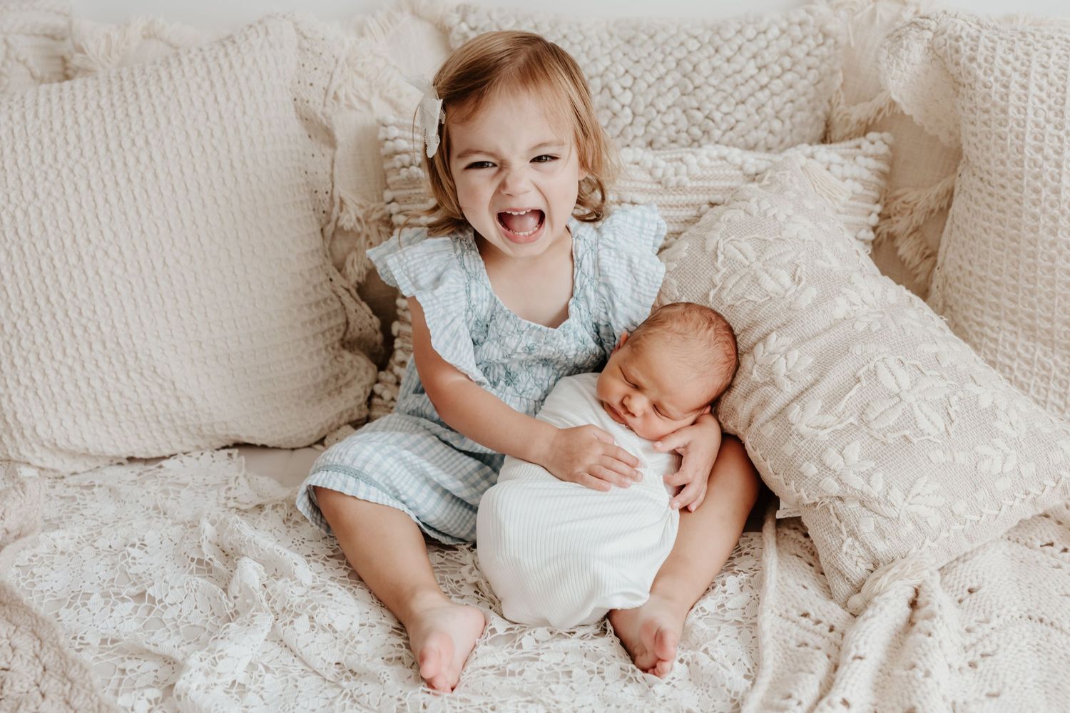 Two young siblings share joyful moments together on a white bed.