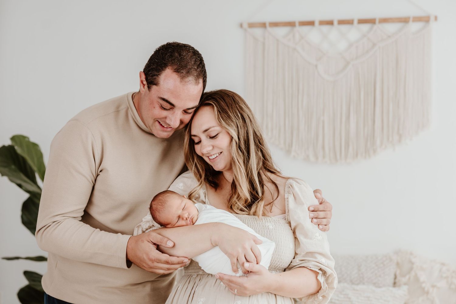 A tender family moment with a newborn baby in a cozy room with macrame wall decor.
