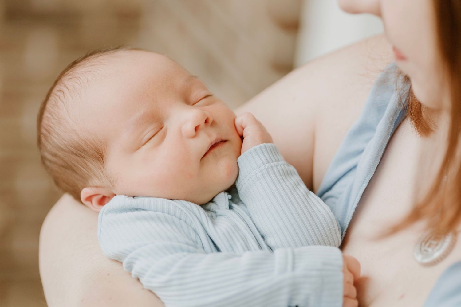 Sleeping newborn baby in light blue clothing being cradled gently.