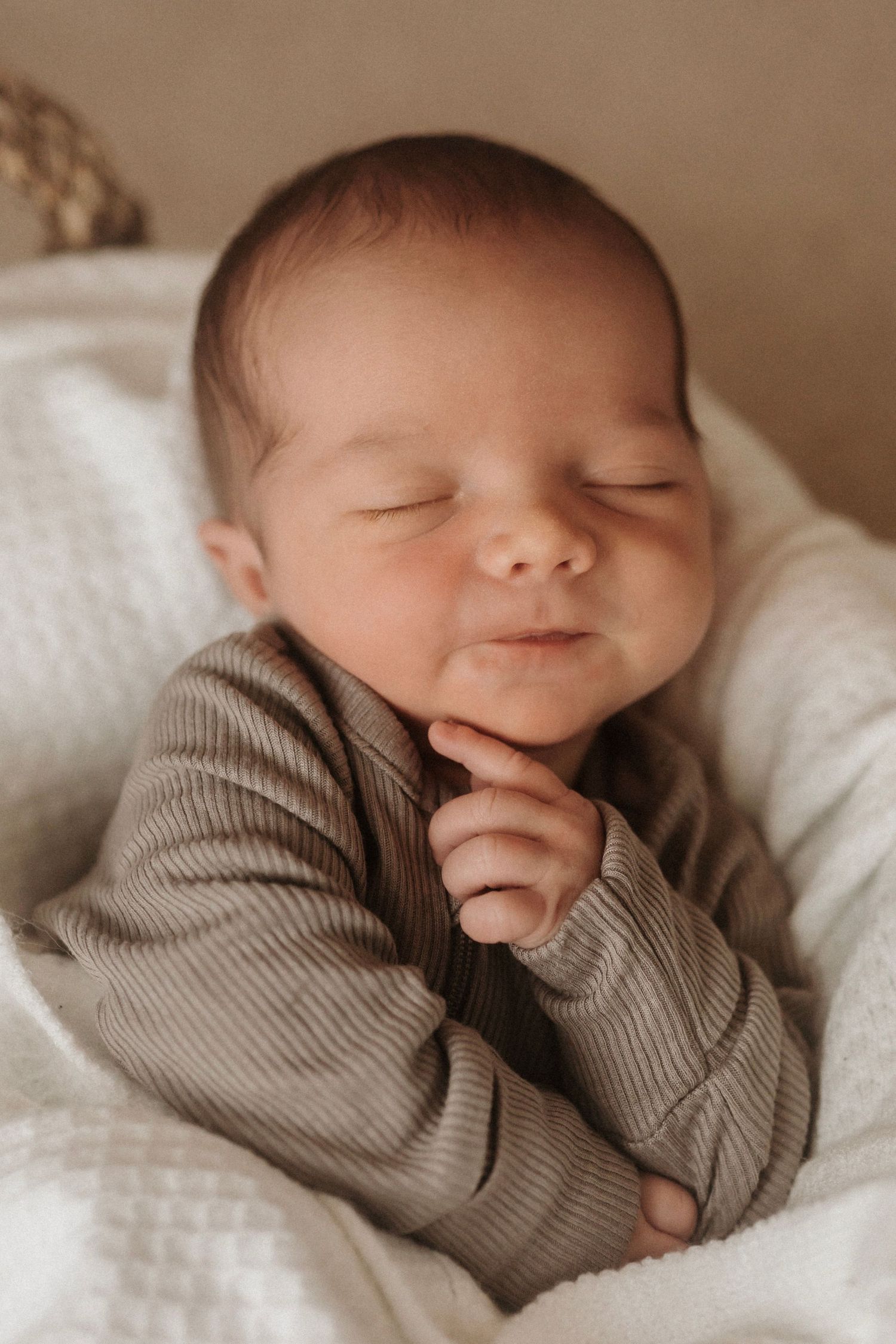 Peaceful sleeping newborn baby in gray outfit resting on white bedding.