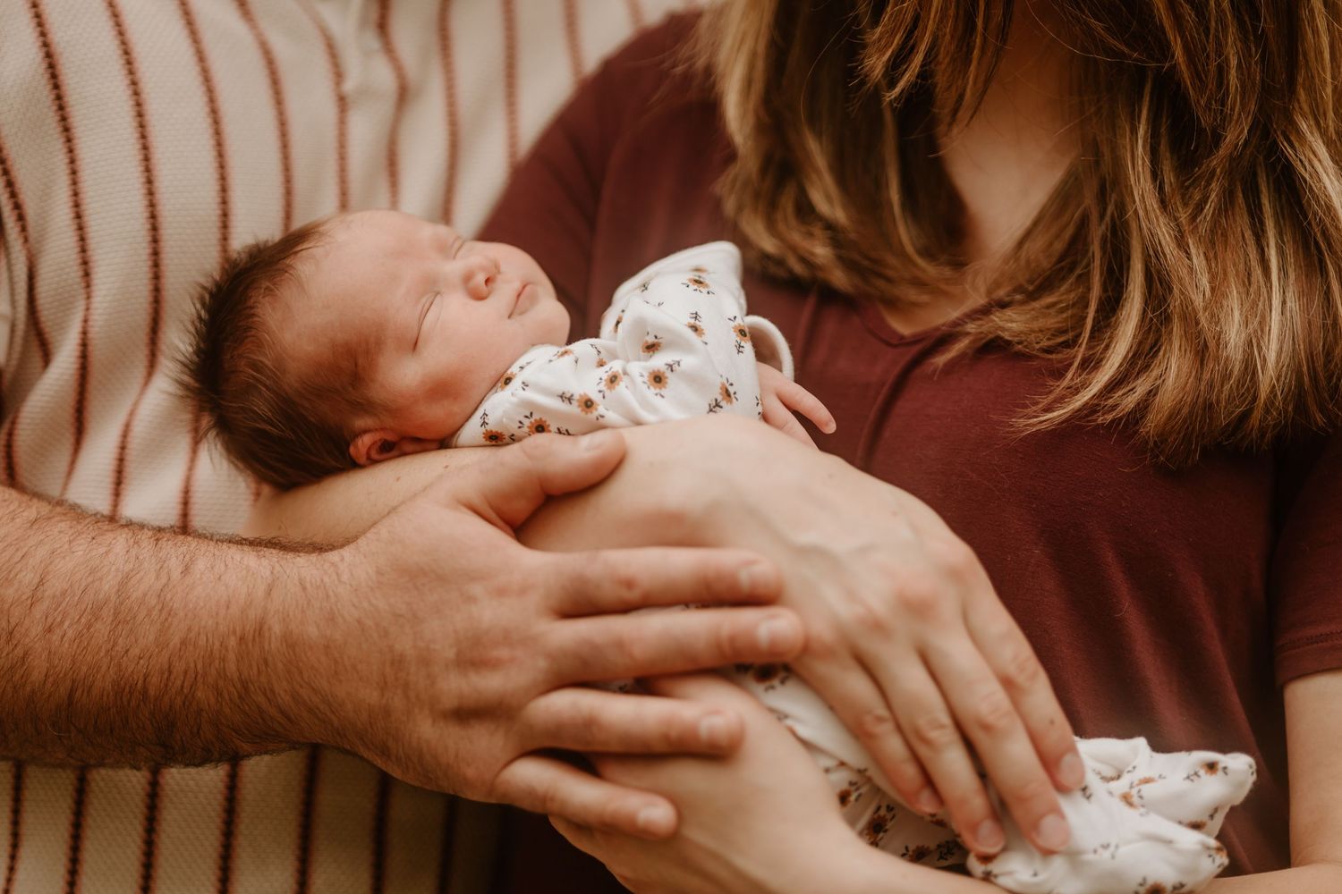 Sleeping newborn baby in patterned outfit being held by caring hands.