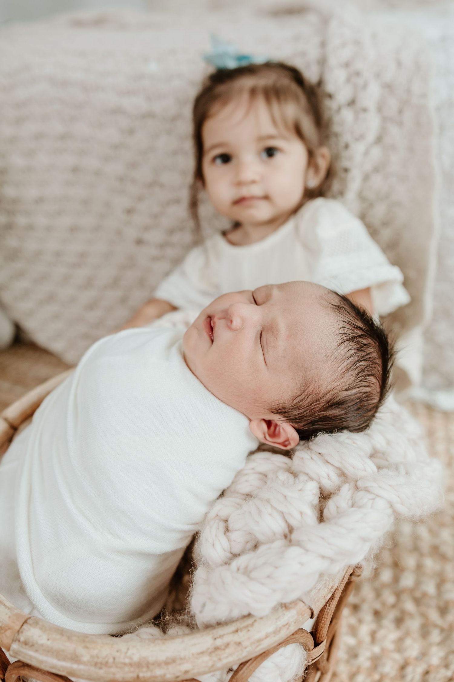 A tender sibling moment with newborn baby lying on textured blanket.