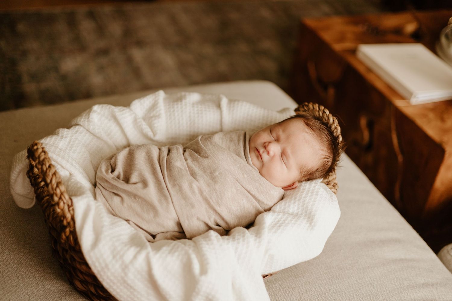 A sleeping newborn wrapped in white fabric rests on a textured surface in warm lighting.