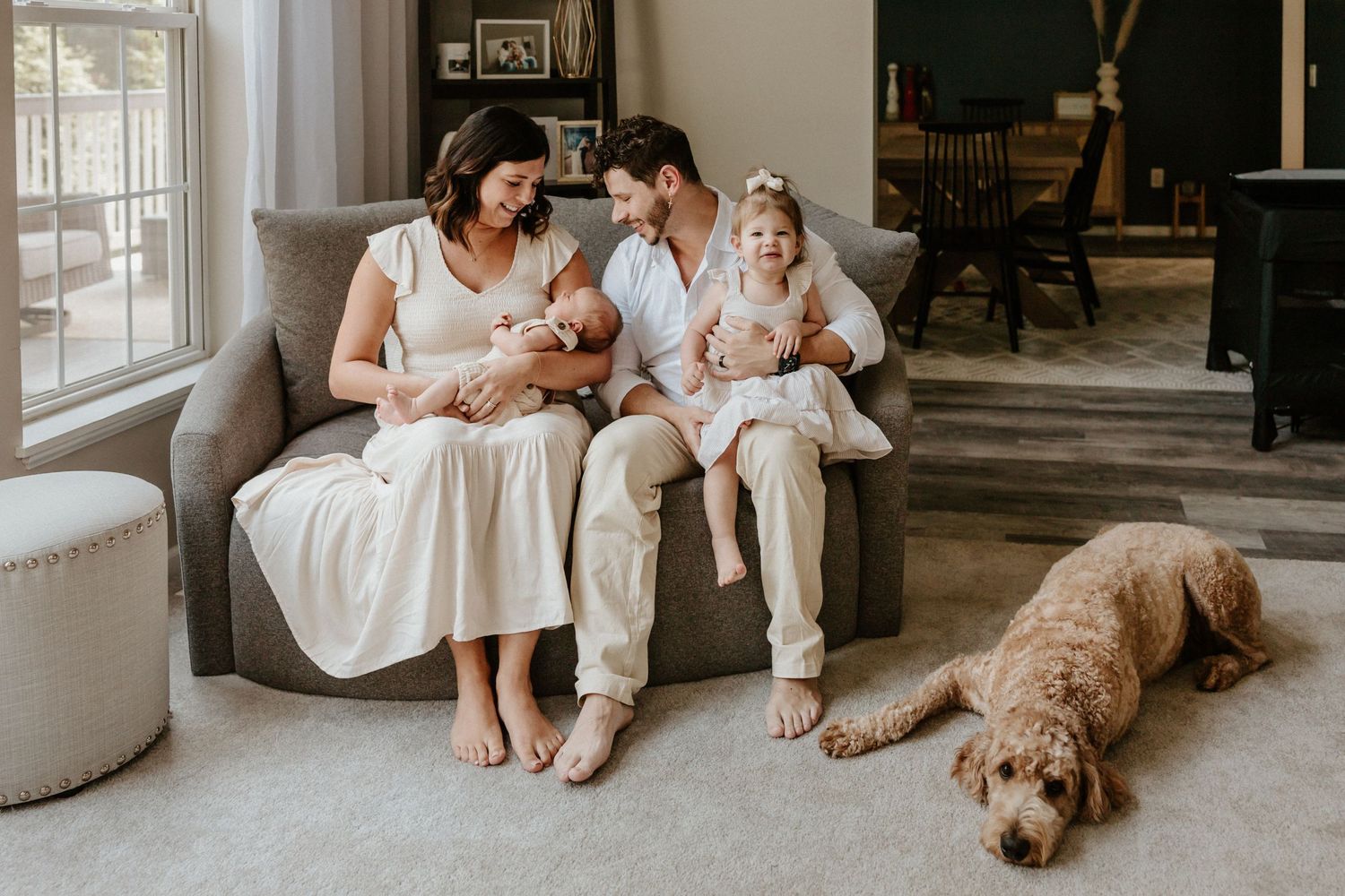 Family relaxing on couch with baby and dog in bright living room with natural light.
