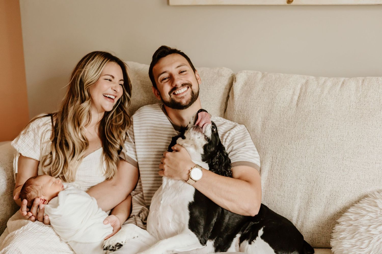 Joyful family moment on couch with newborn baby and black and white pet dog.