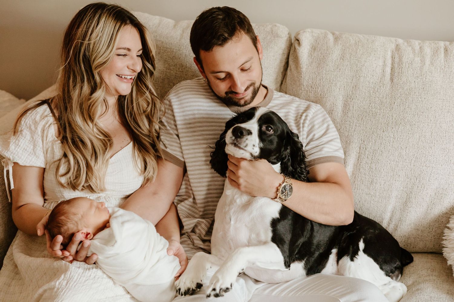 Family portrait with newborn baby and black and white dog on cream colored couch.