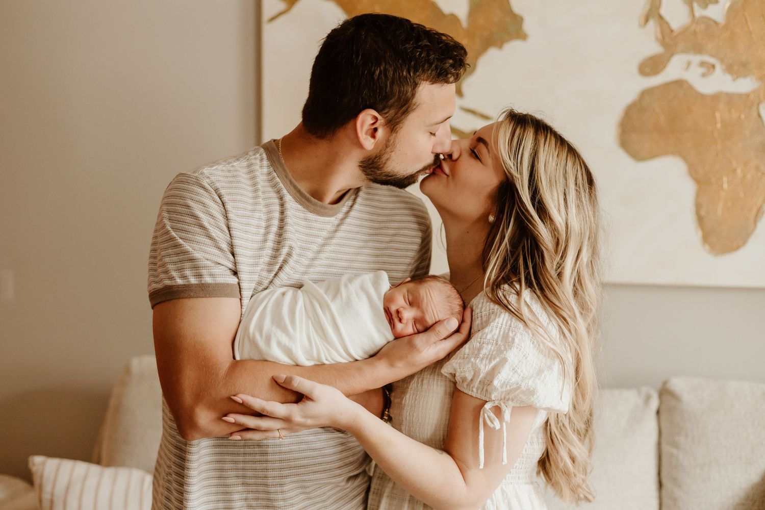 Intimate family moment with newborn against backdrop of golden world map wall art.