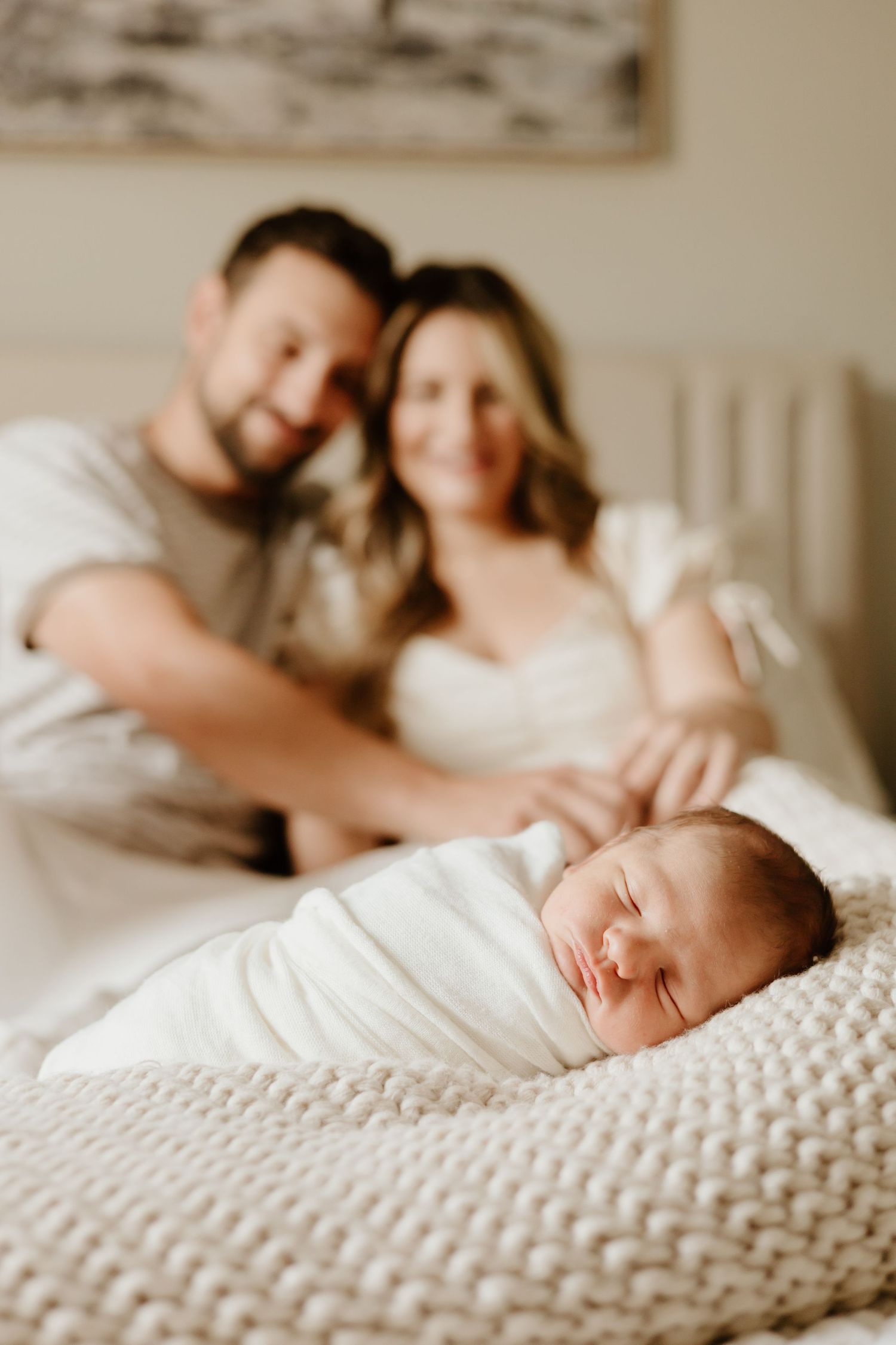 Sweet newborn photography session with sleeping baby in white wrap on textured bedding.