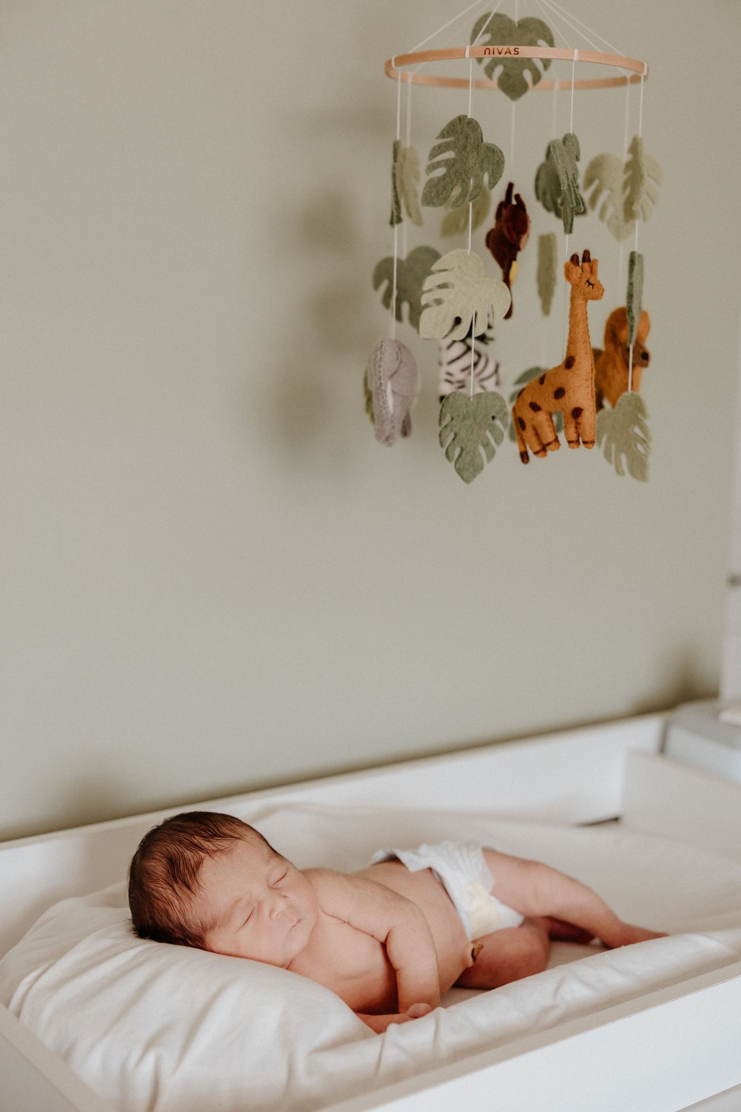 Newborn sleeps on changing table under safari animal mobile in nursery.