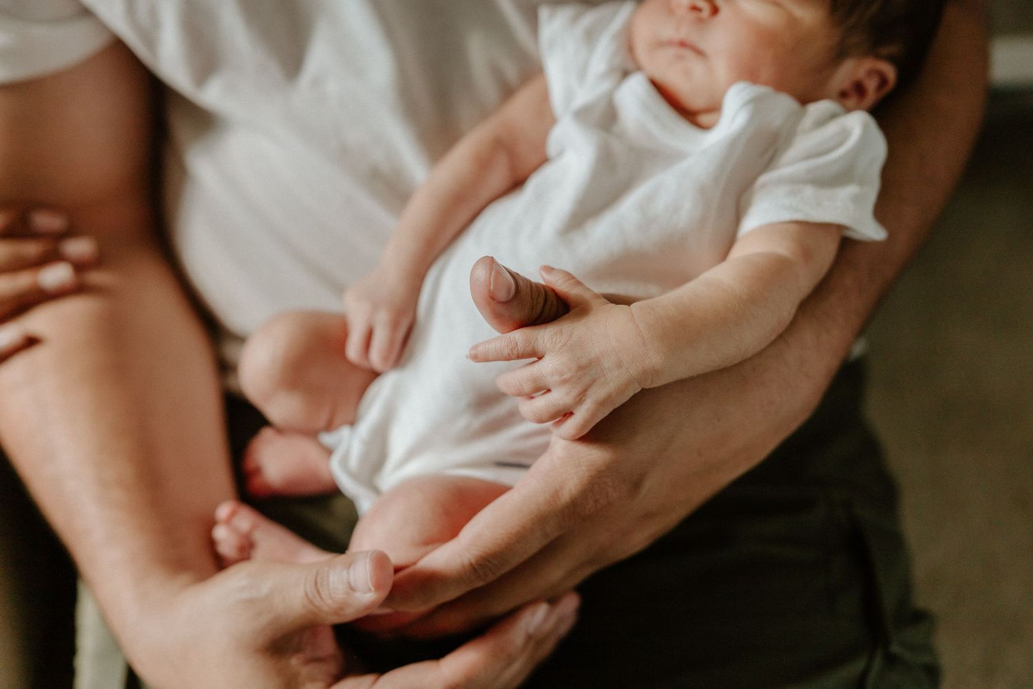 A newborn baby wearing white clothing rests gently in caring hands.