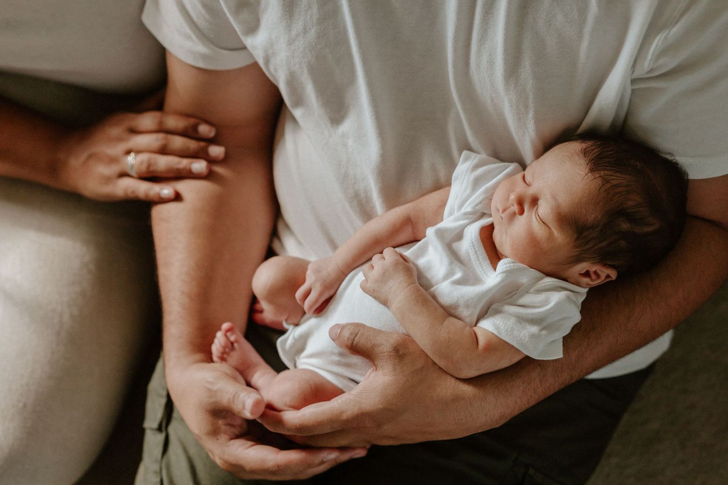 A tiny infant in white clothing sleeps peacefully while being cradled.