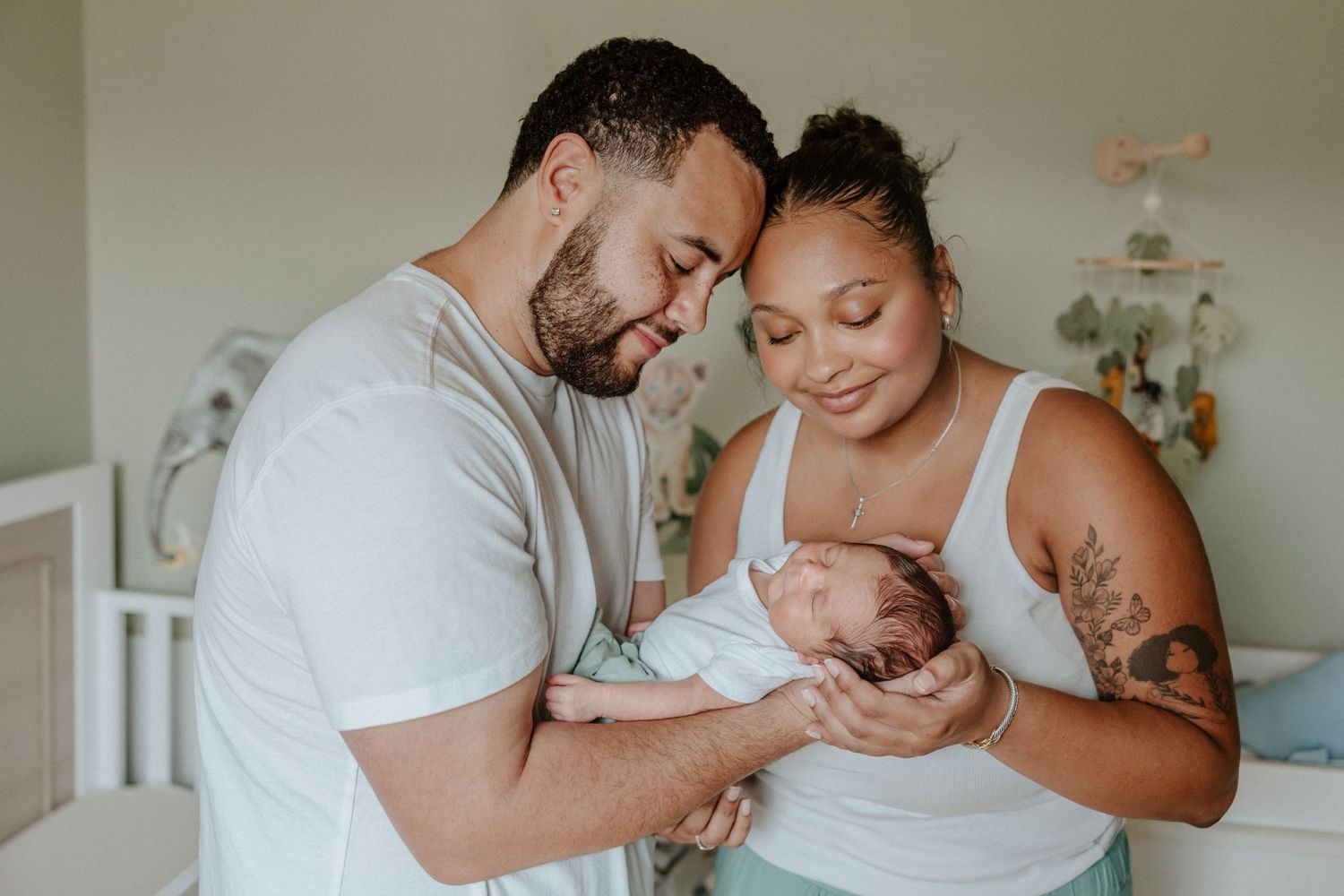 Parents share tender moment while holding sleeping newborn in nursery.