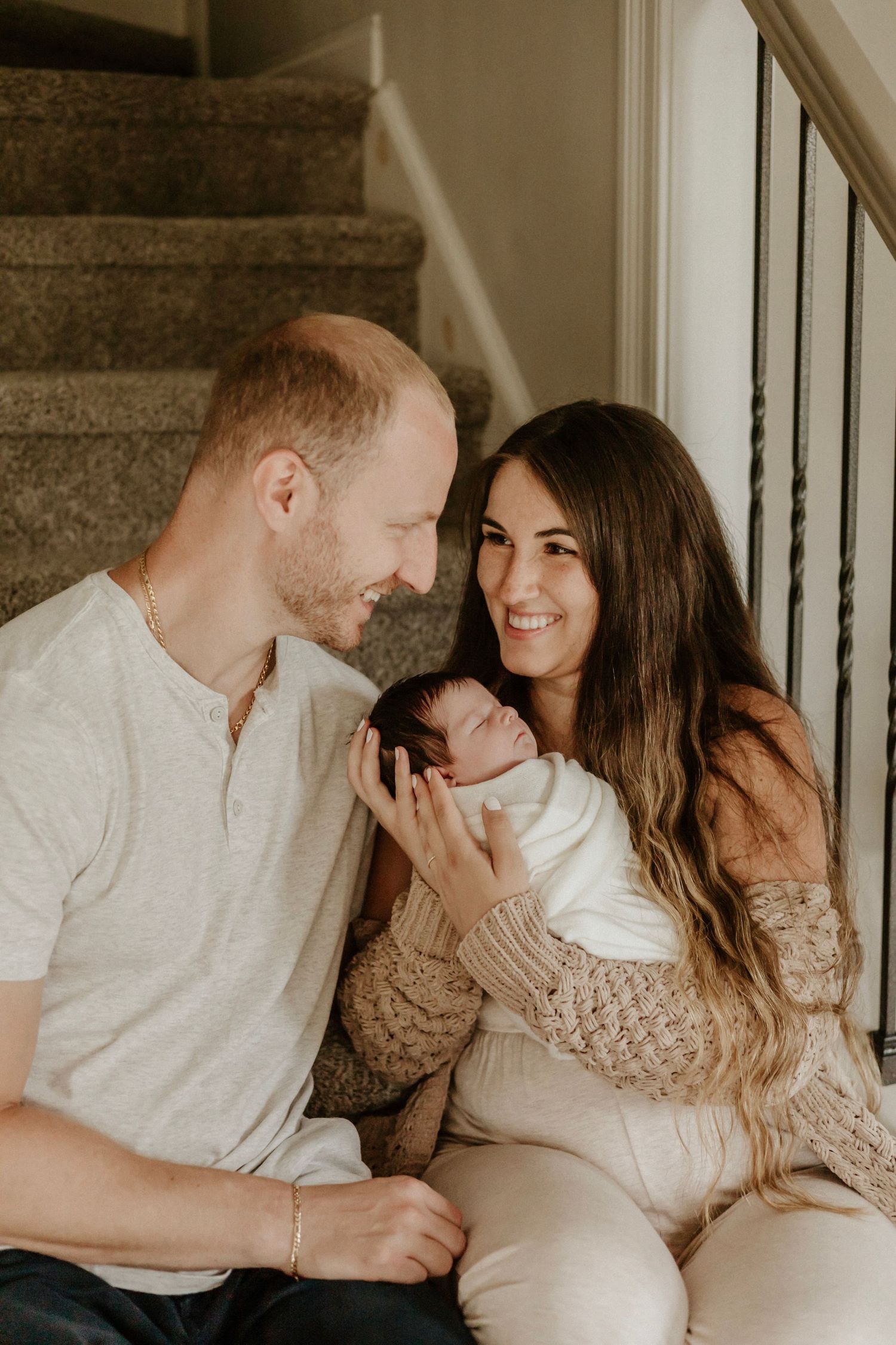A loving family moment on carpeted stairs as parents gaze adoringly at their newborn baby.