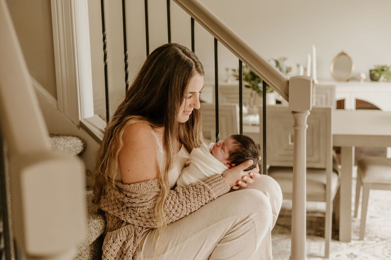 A tender moment captured on stairs as a new parent cradles their newborn baby in a cozy knit sweater.