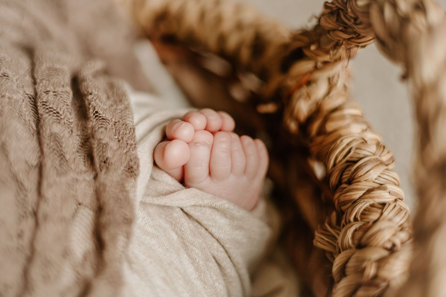 Close-up photo of a tiny newborn baby's hand wrapped in a soft beige blanket.