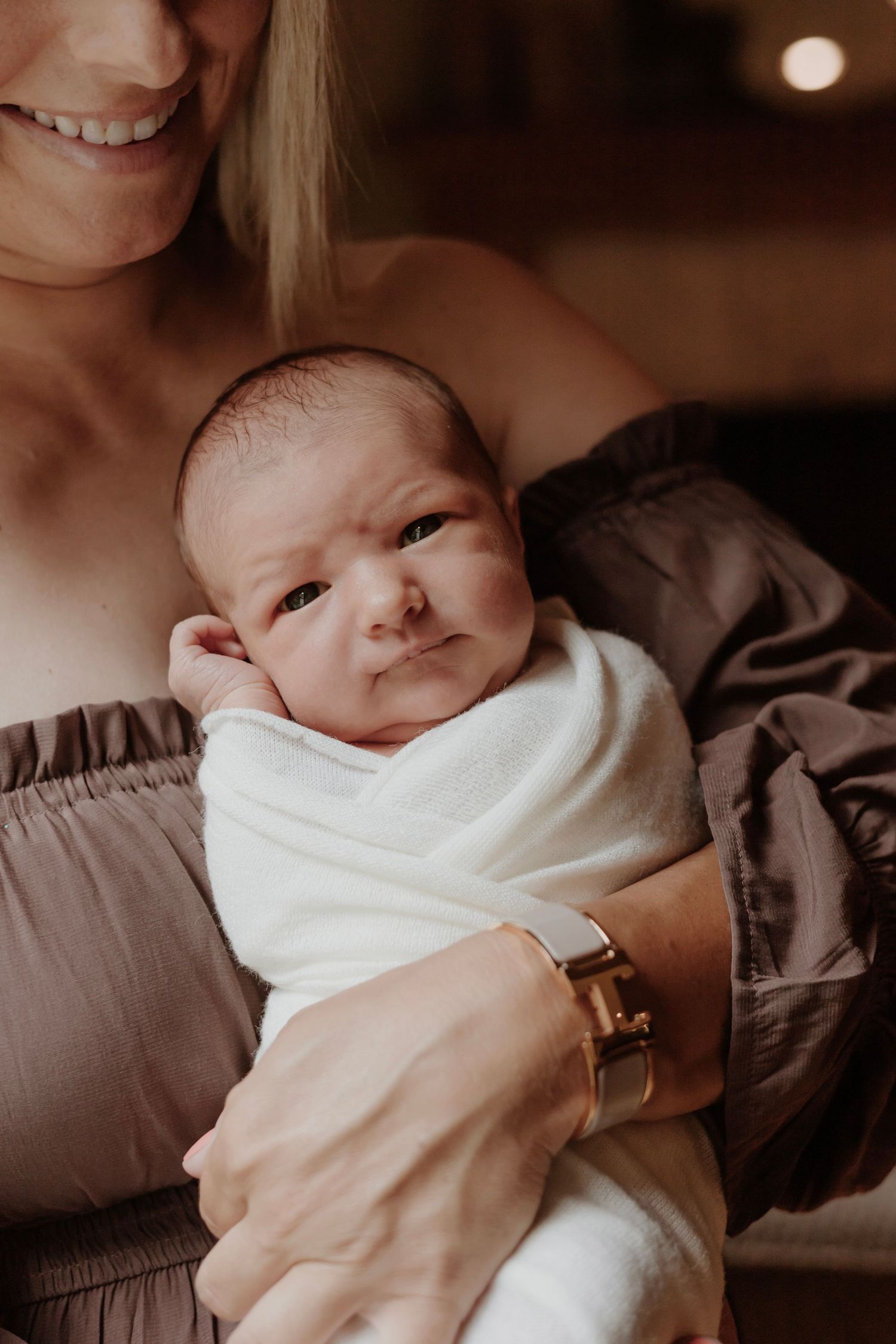 Newborn baby wrapped in white blanket looking up while being held.