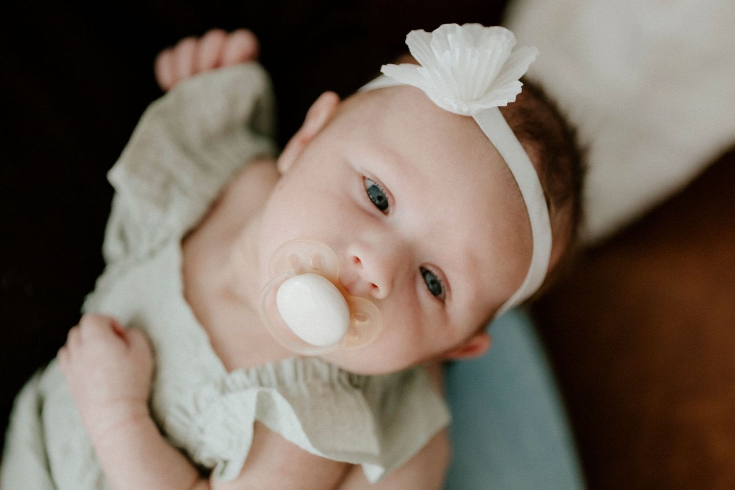Infant wearing white headband and mint green outfit resting on soft fabric.