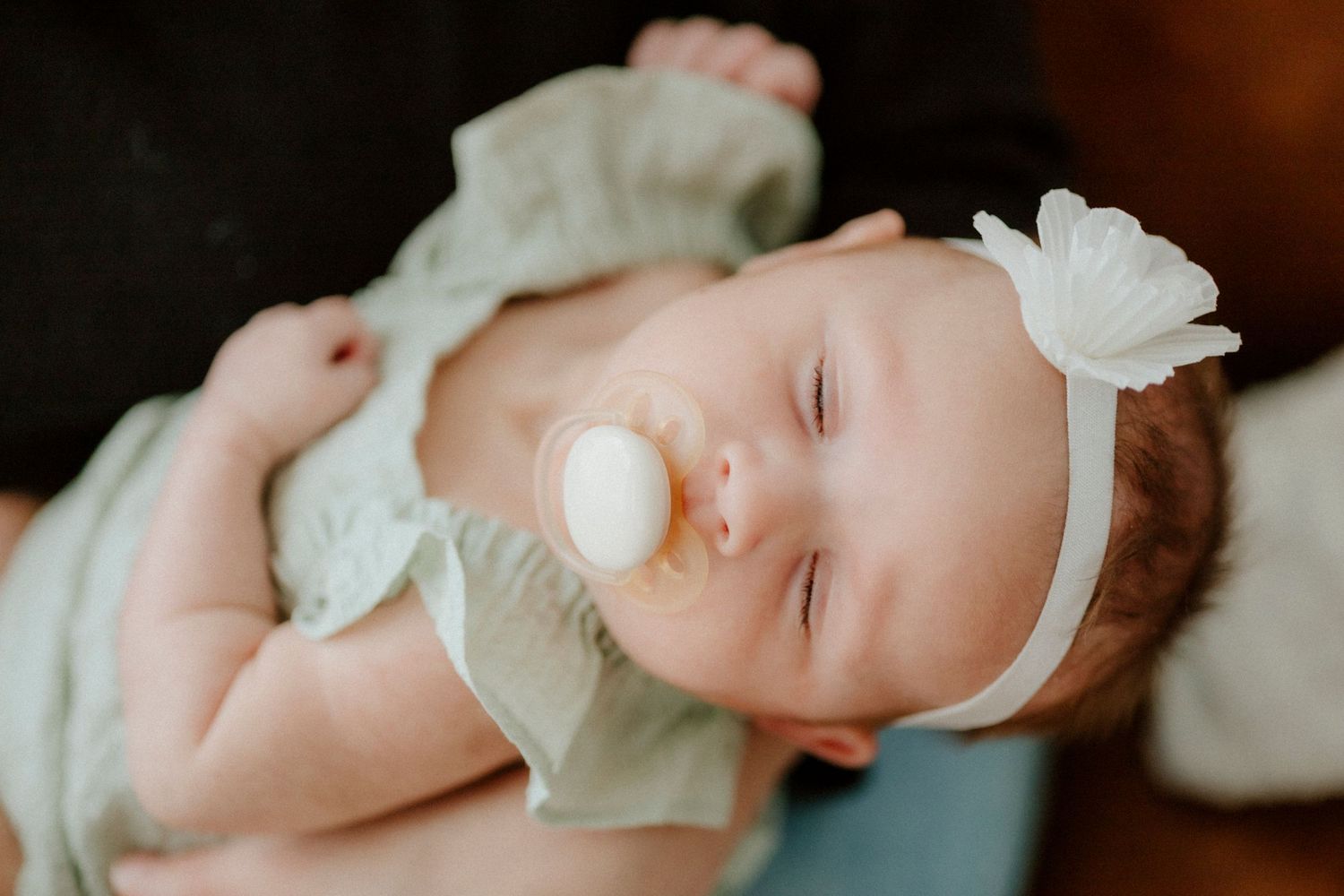 Sleeping infant in mint green outfit with white bow headband.