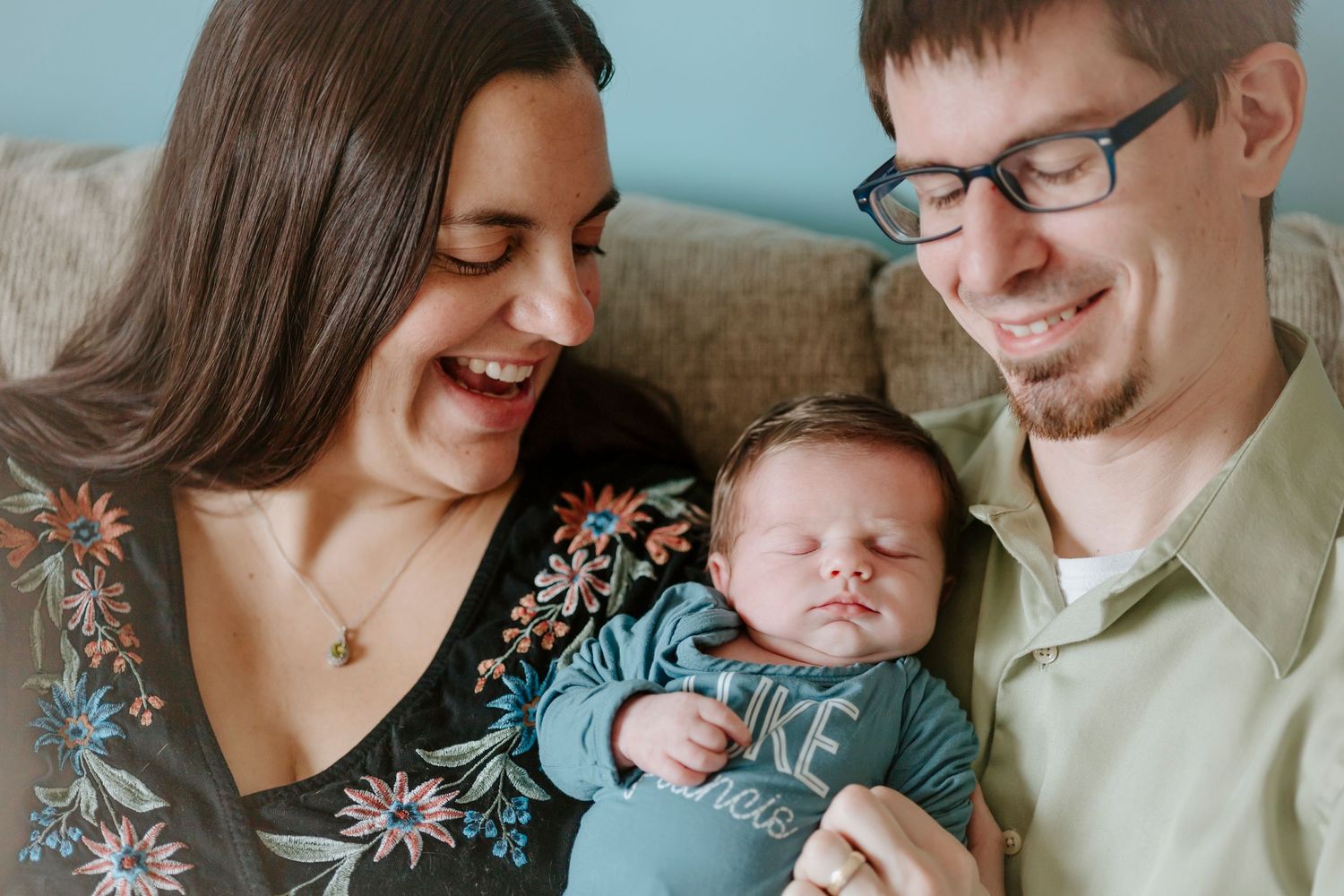 A happy family moment is captured on a couch as they admire their newborn baby wearing blue.