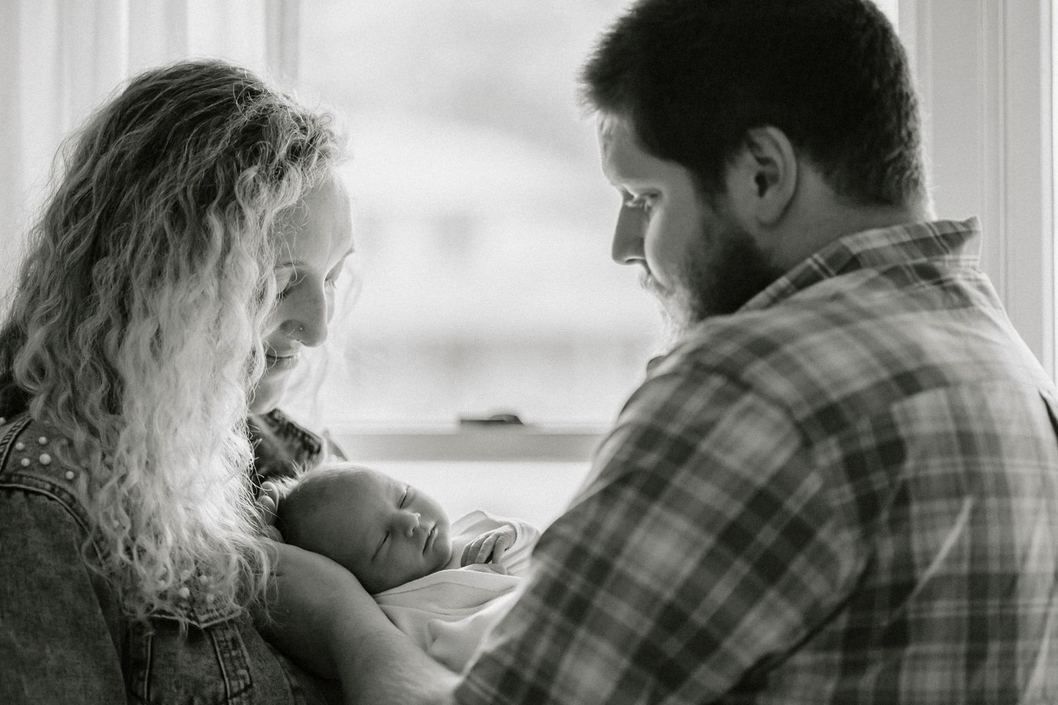 A black and white intimate moment of parents gazing down at their sleeping baby.