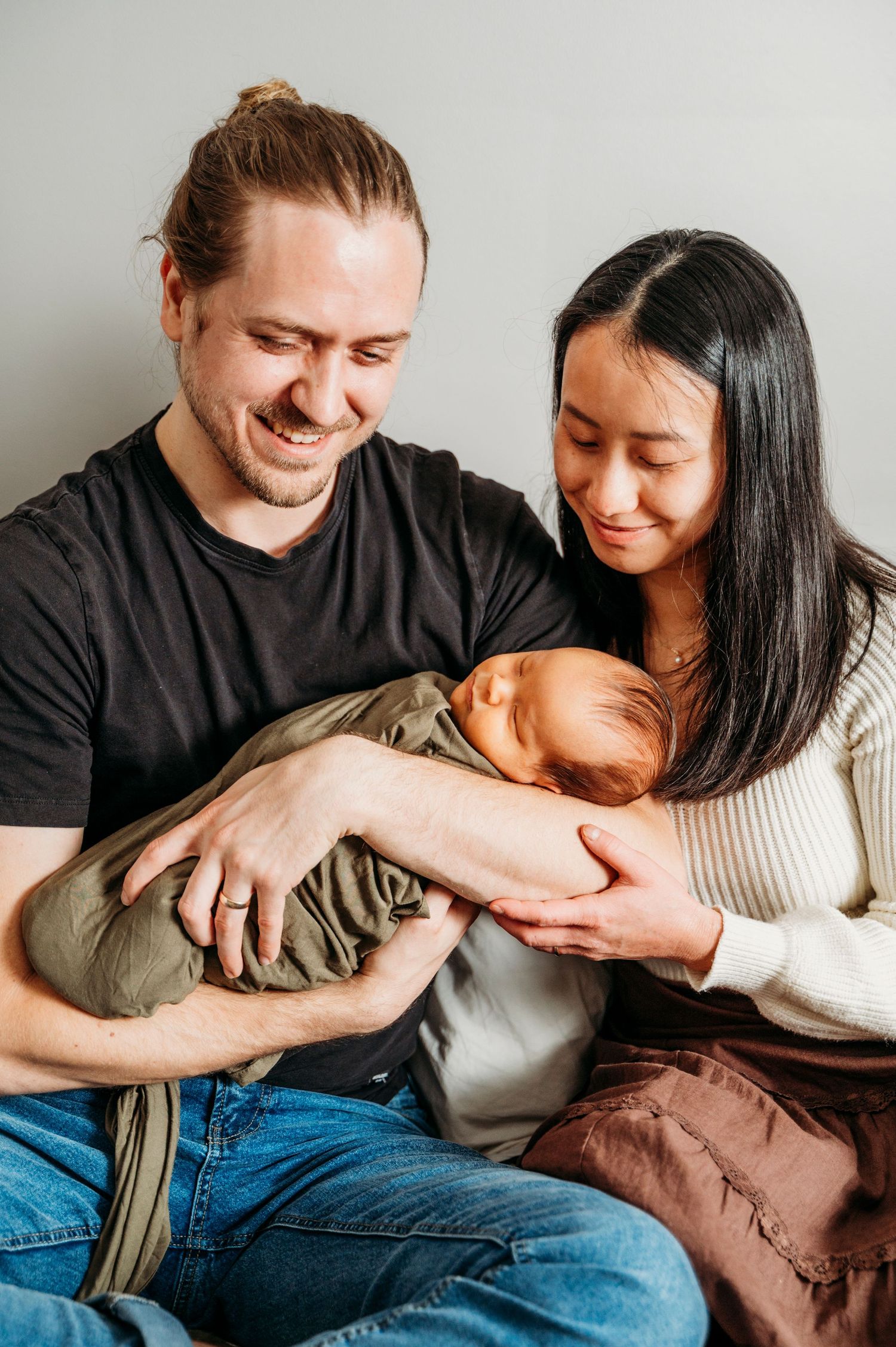 Parents hold newborn baby in their home while smiling.