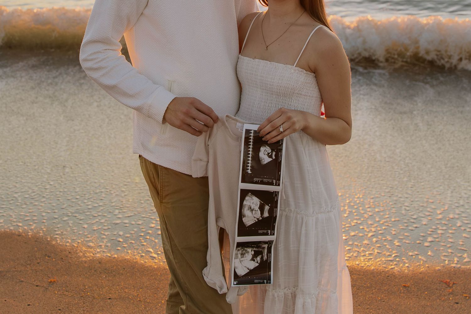 A romantic maternity photoshoot with a couple in casual white attire against a light background.