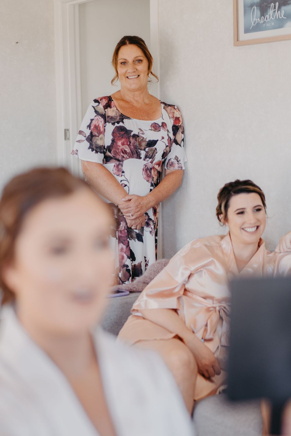 Wedding preparation scene with women in floral dress and robes gathered in bright interior.