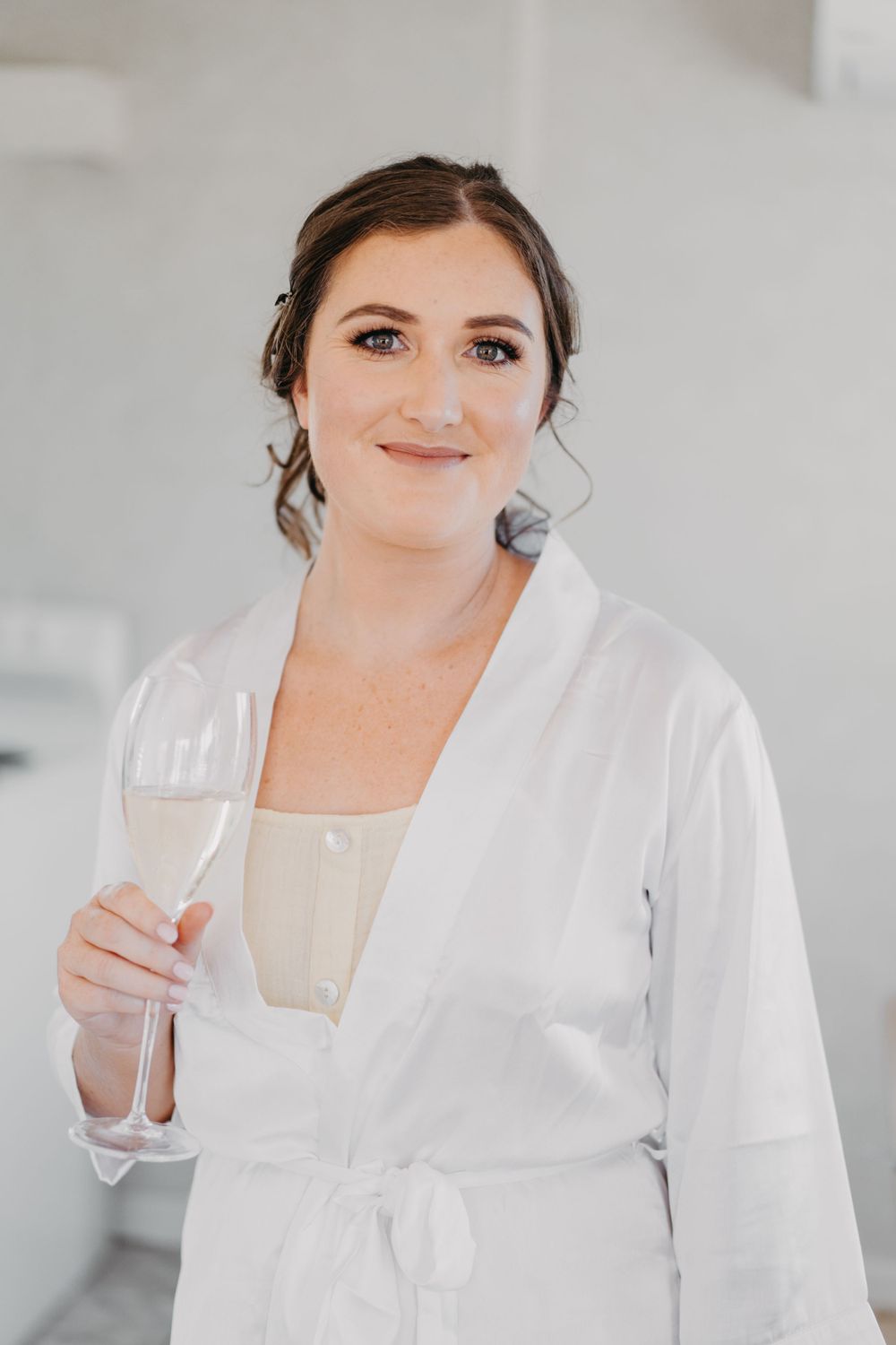 Person in white robe holds champagne glass during wedding morning preparations.