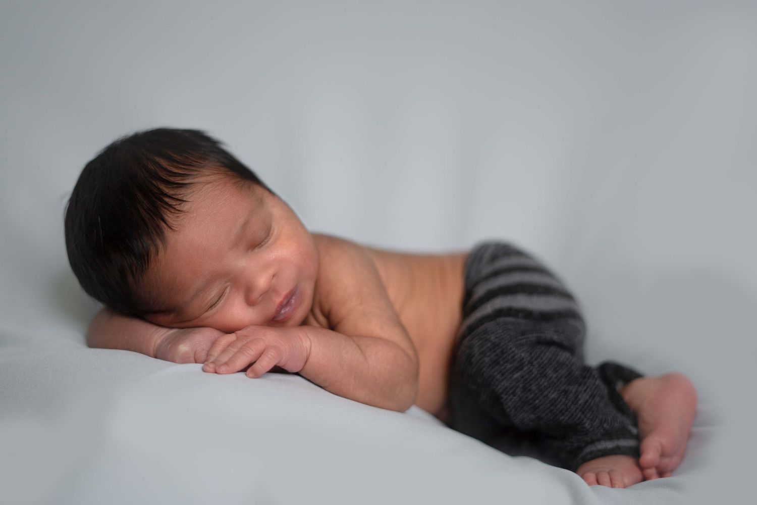 Sleeping newborn in soft brown knitted bunny outfit on beige blanket.