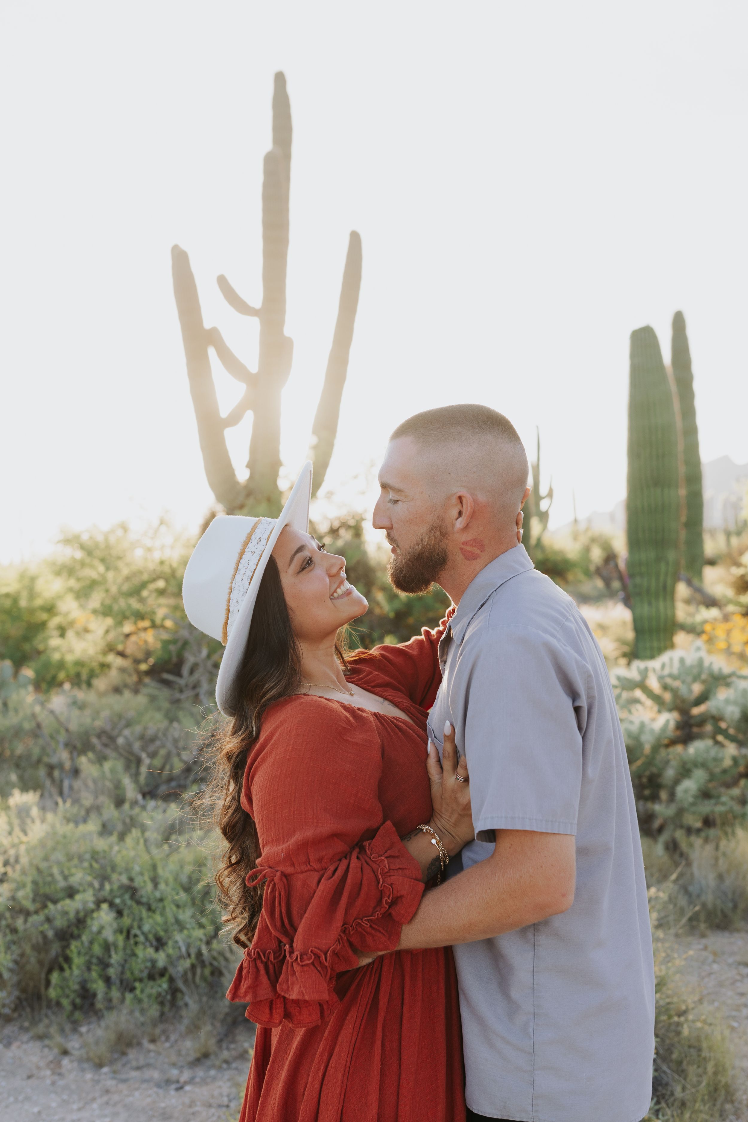 A romantic desert photoshoot with a couple embracing among towering saguaro cacti.
