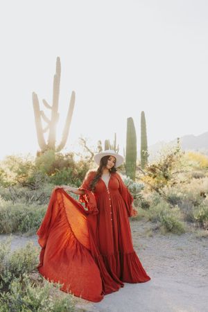 A woman in a flowing red dress twirls in a desert landscape with saguaro cacti.