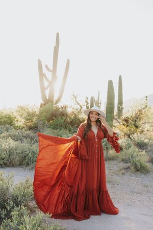 A woman in a dramatic red dress poses with flowing fabric among desert cacti.
